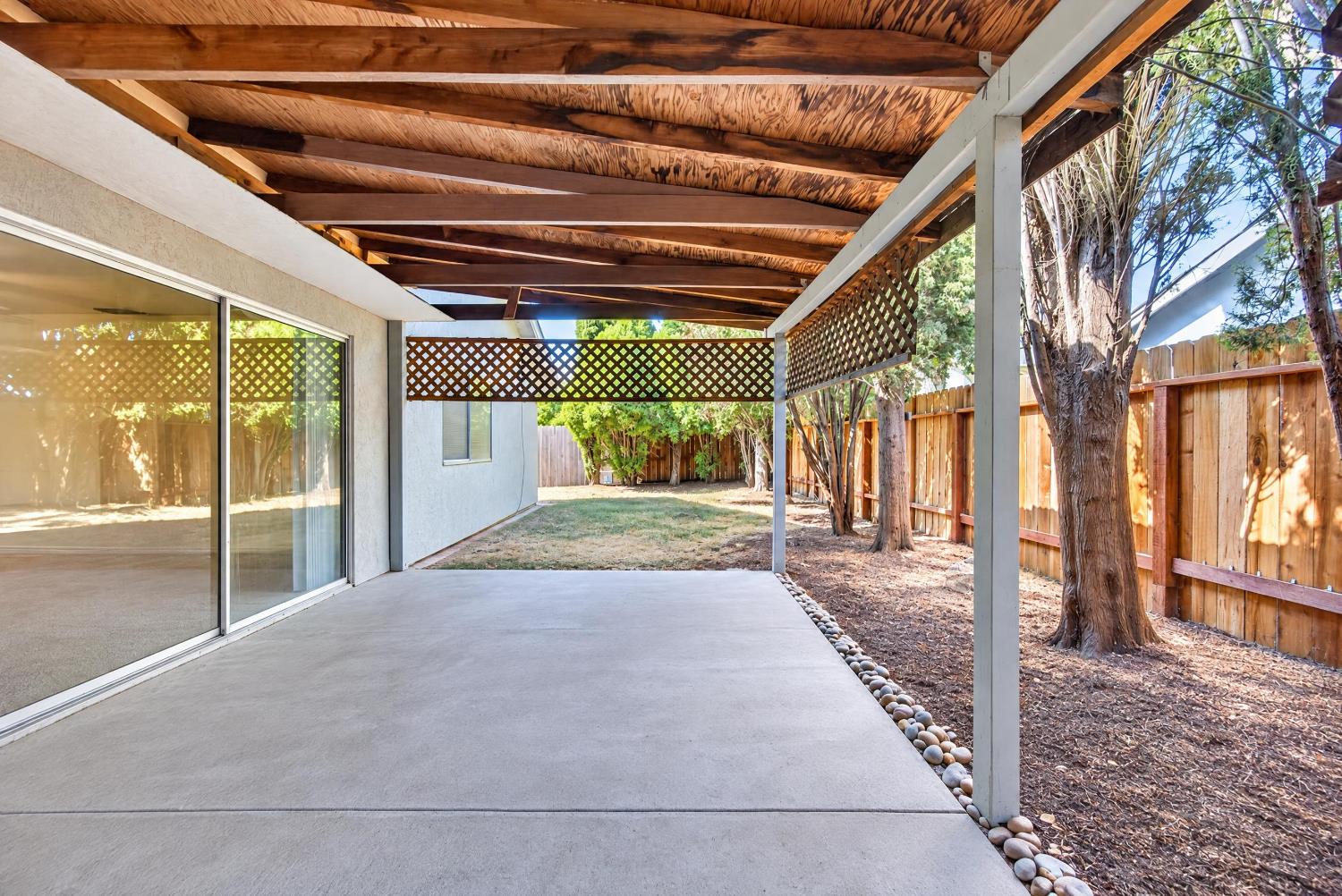 Covered concrete patio with exposed wood beams, lattice screens, and sliding glass doors.