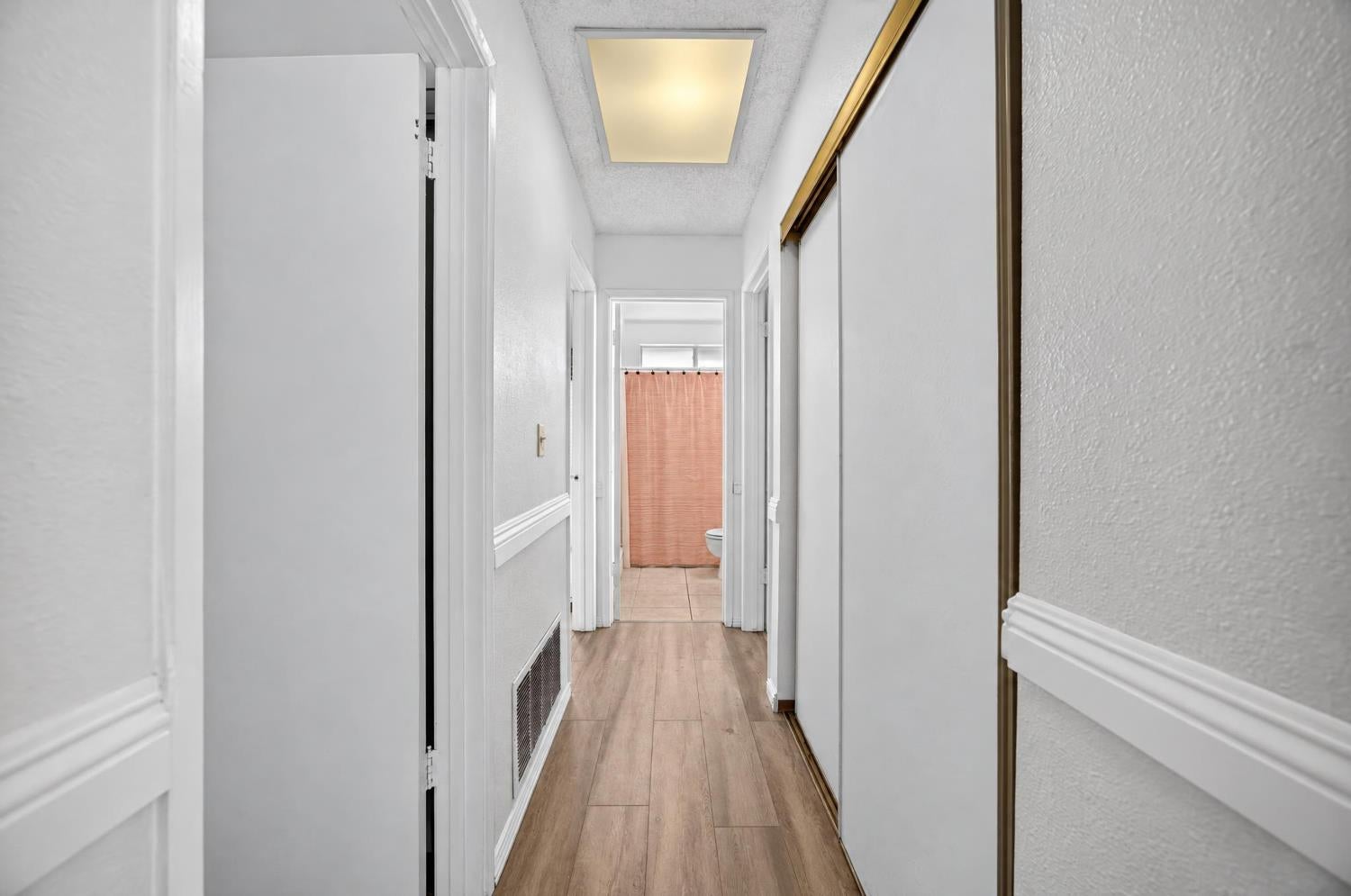 Hallway with wood-look flooring and sliding closet doors, leading to a bathroom with a peach shower curtain.