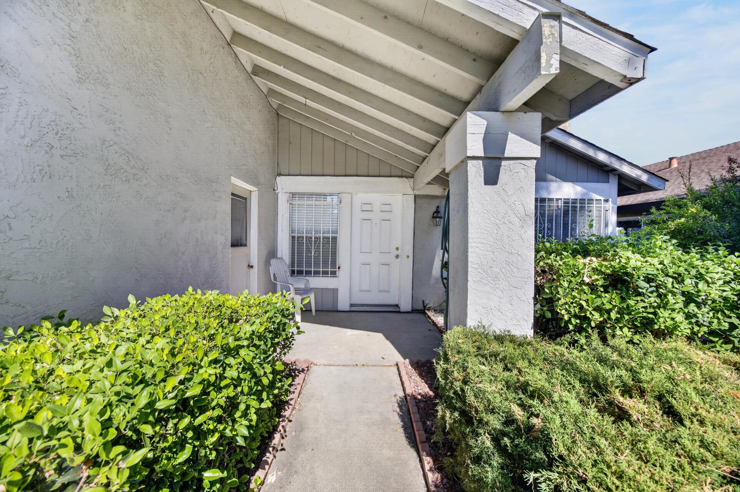 Home’s recessed front entrance beneath a covered porch, approached by a walkway between green hedges.