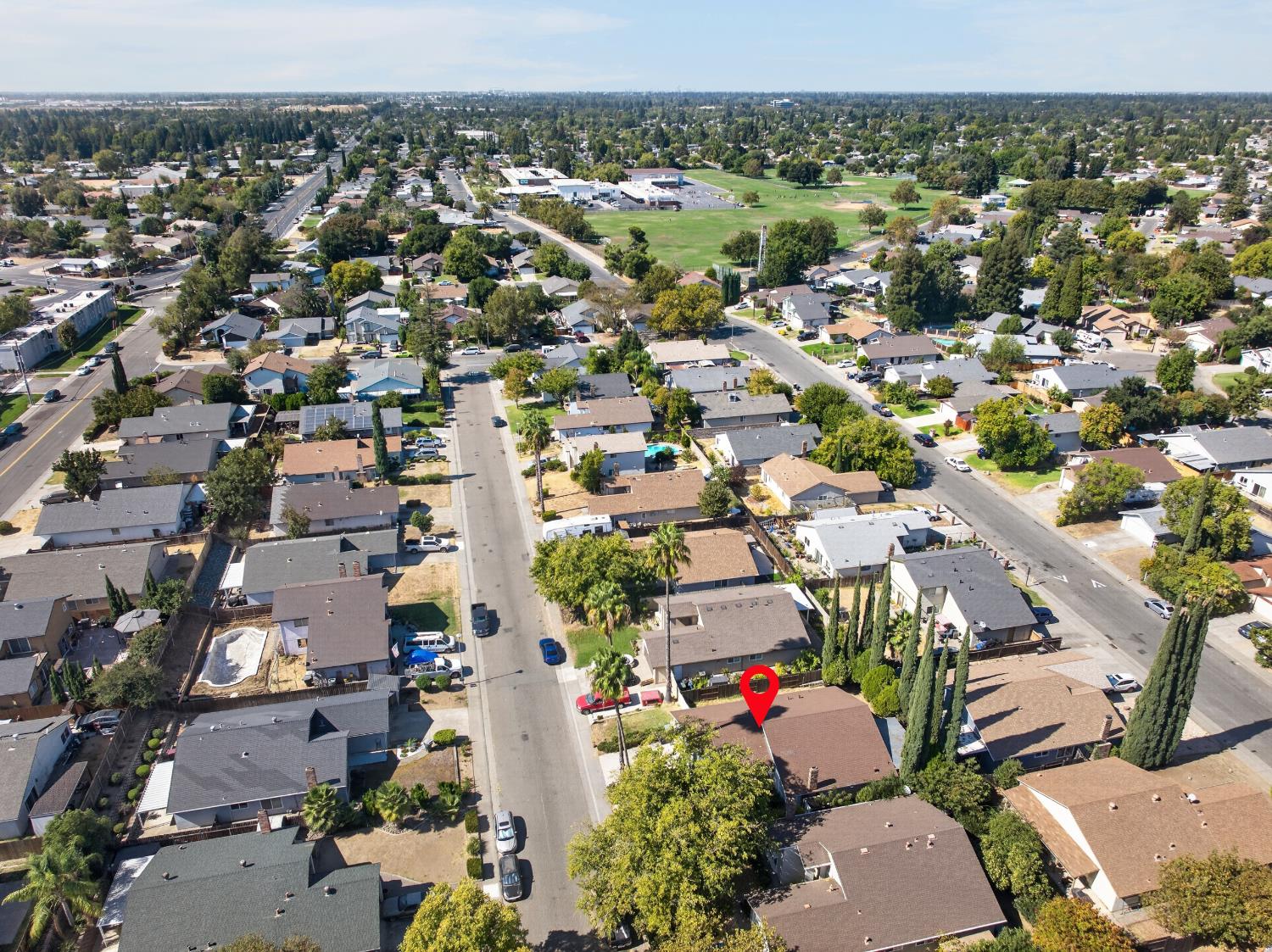 Aerial view of a residential neighborhood, with a red marker over one home and a green open space beyond.