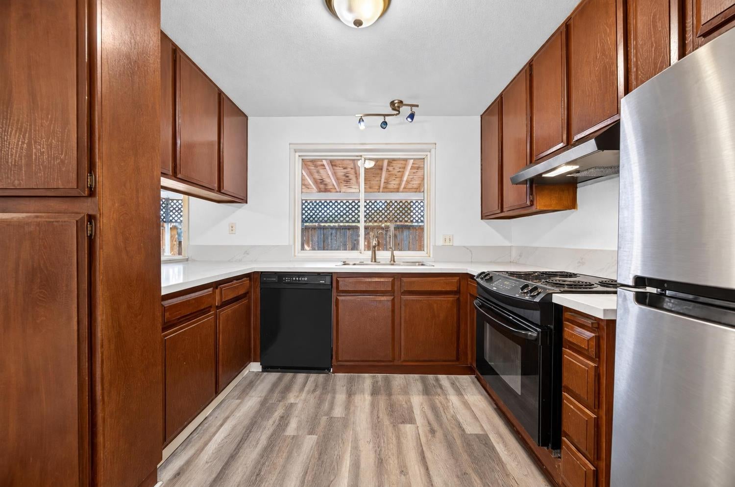 Kitchen with dark wood cabinets, white counters, and a window above the sink.