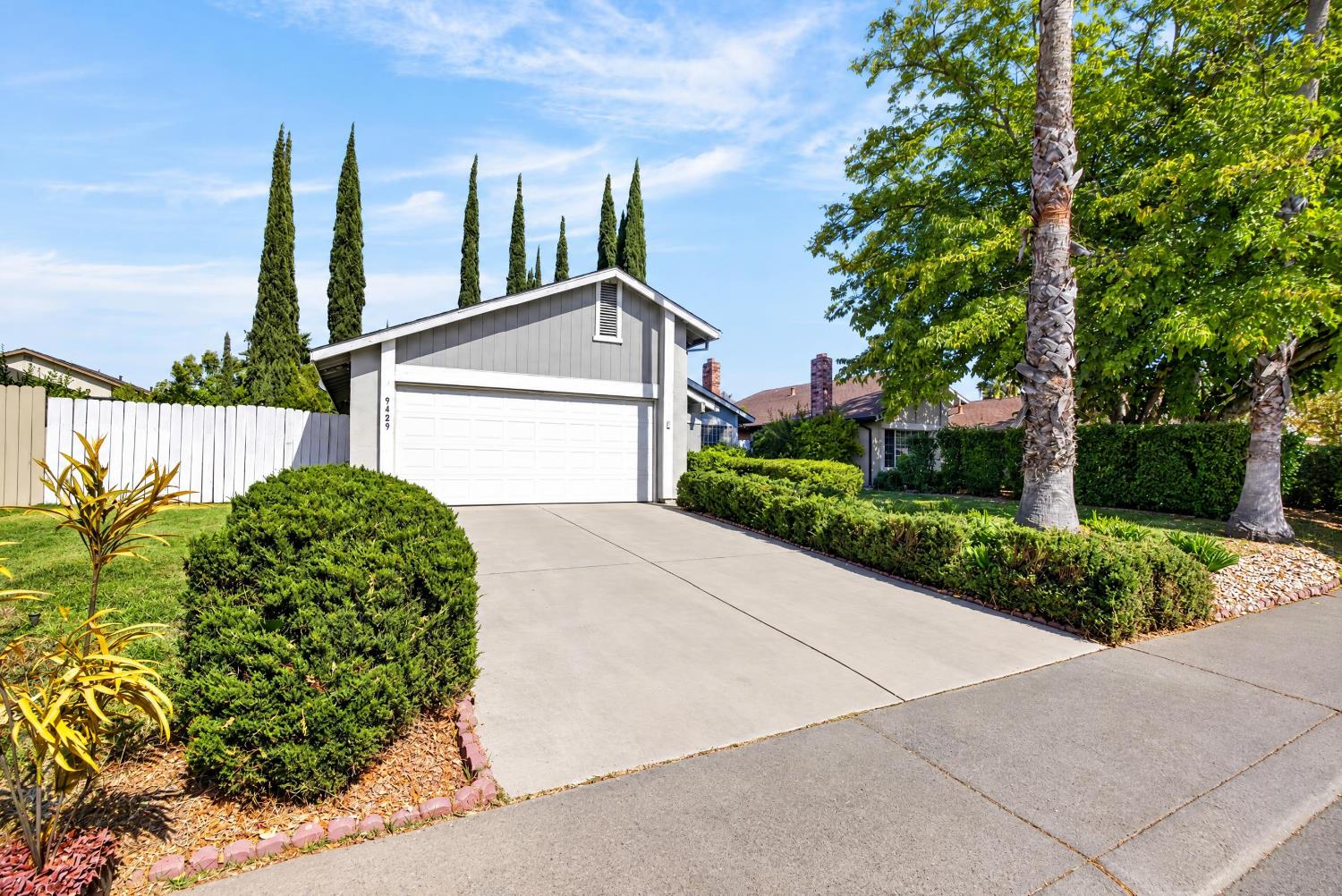 Gray home with a white double garage, landscaped yard, and wide concrete driveway.