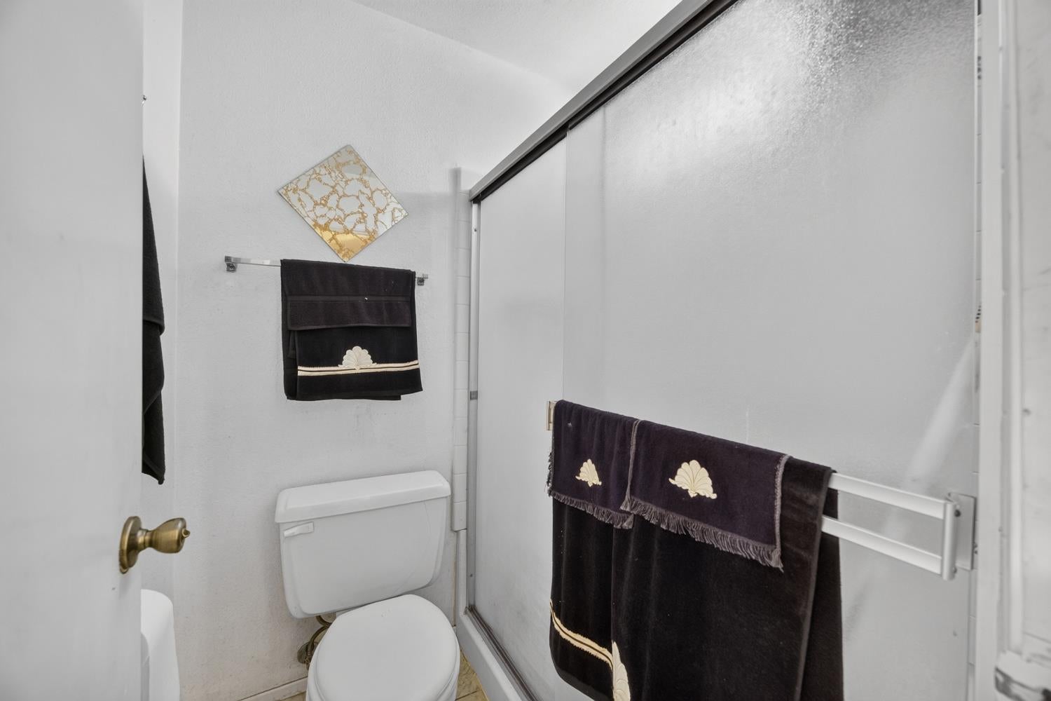 Bathroom with a toilet, sliding glass shower, and dark towels with gold trim.