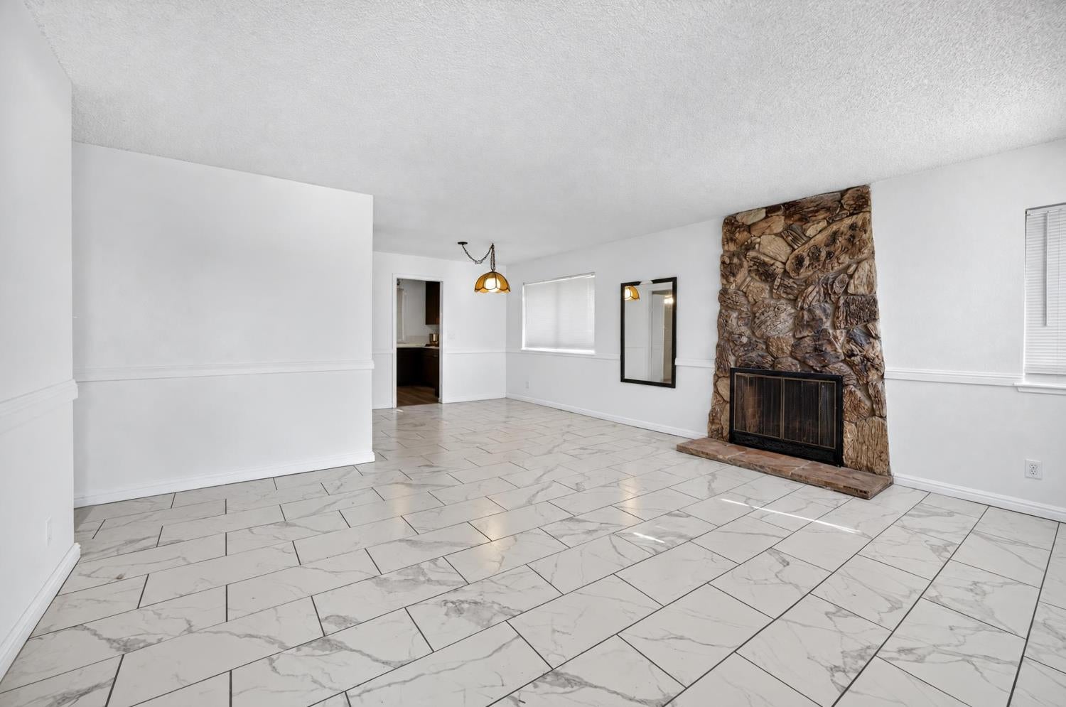 Empty living room with marble-look tile floors and a large stone fireplace.
