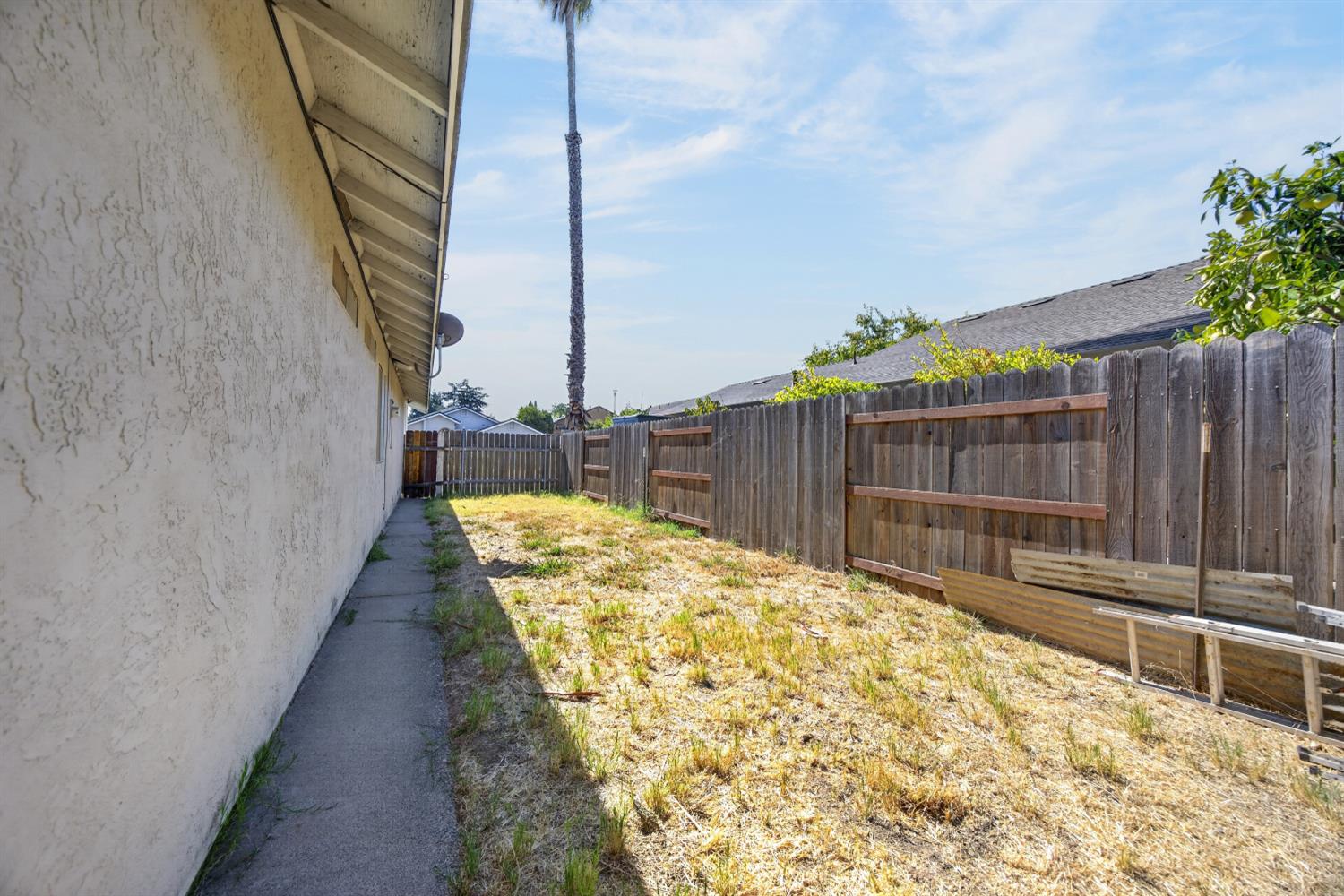 Side yard with dry grass, a concrete walkway, and a tall wooden privacy fence.