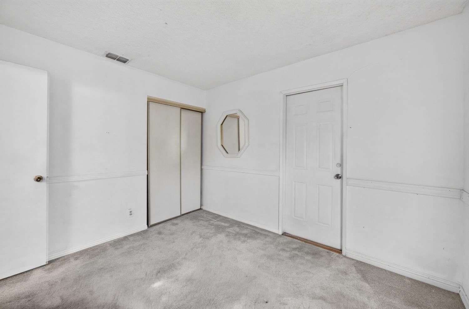 Empty bedroom with gray carpet, a sliding-door closet, and a small octagonal mirror.