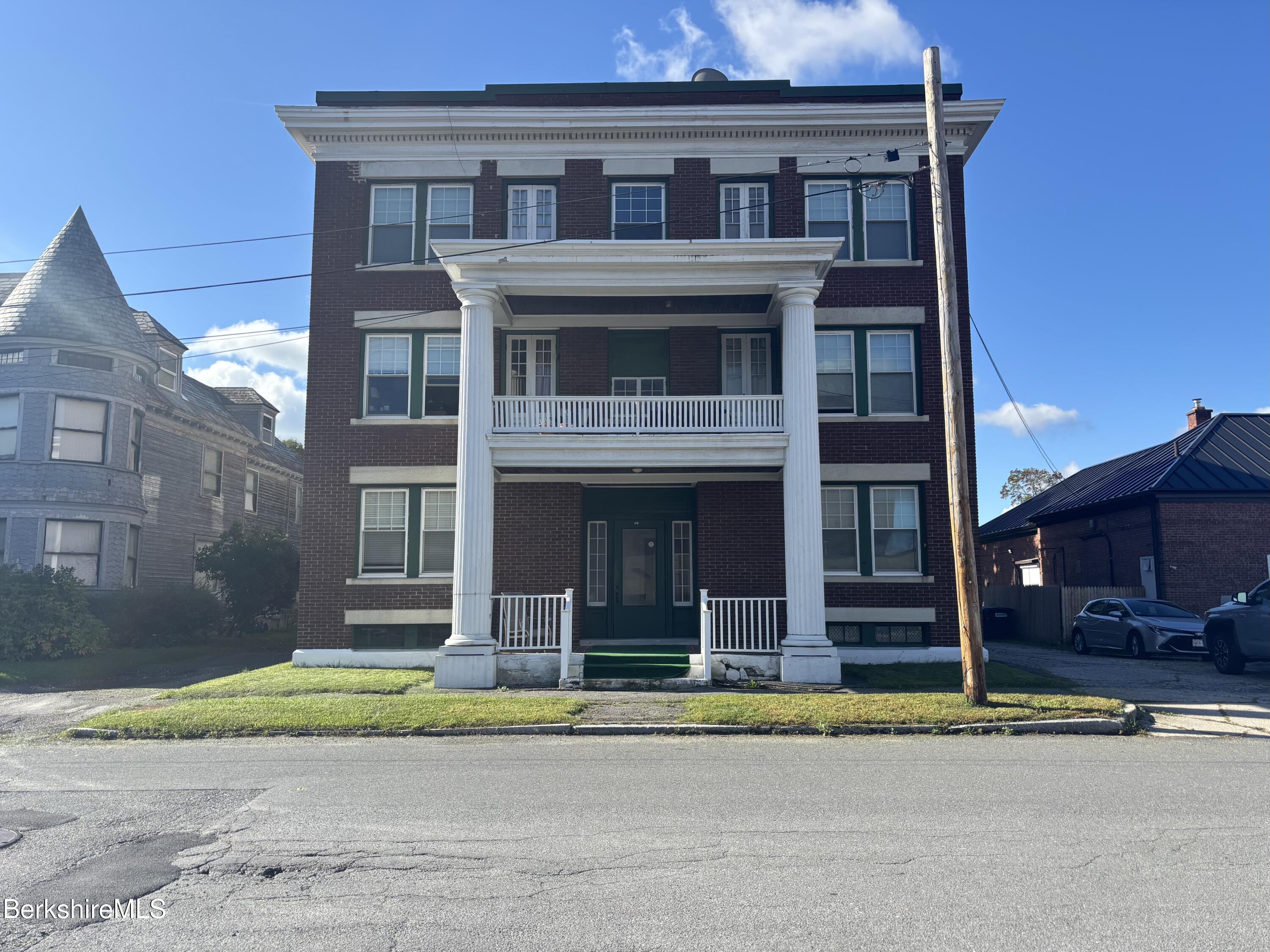 Three-story brick building with white columns framing its entrance and balconies.