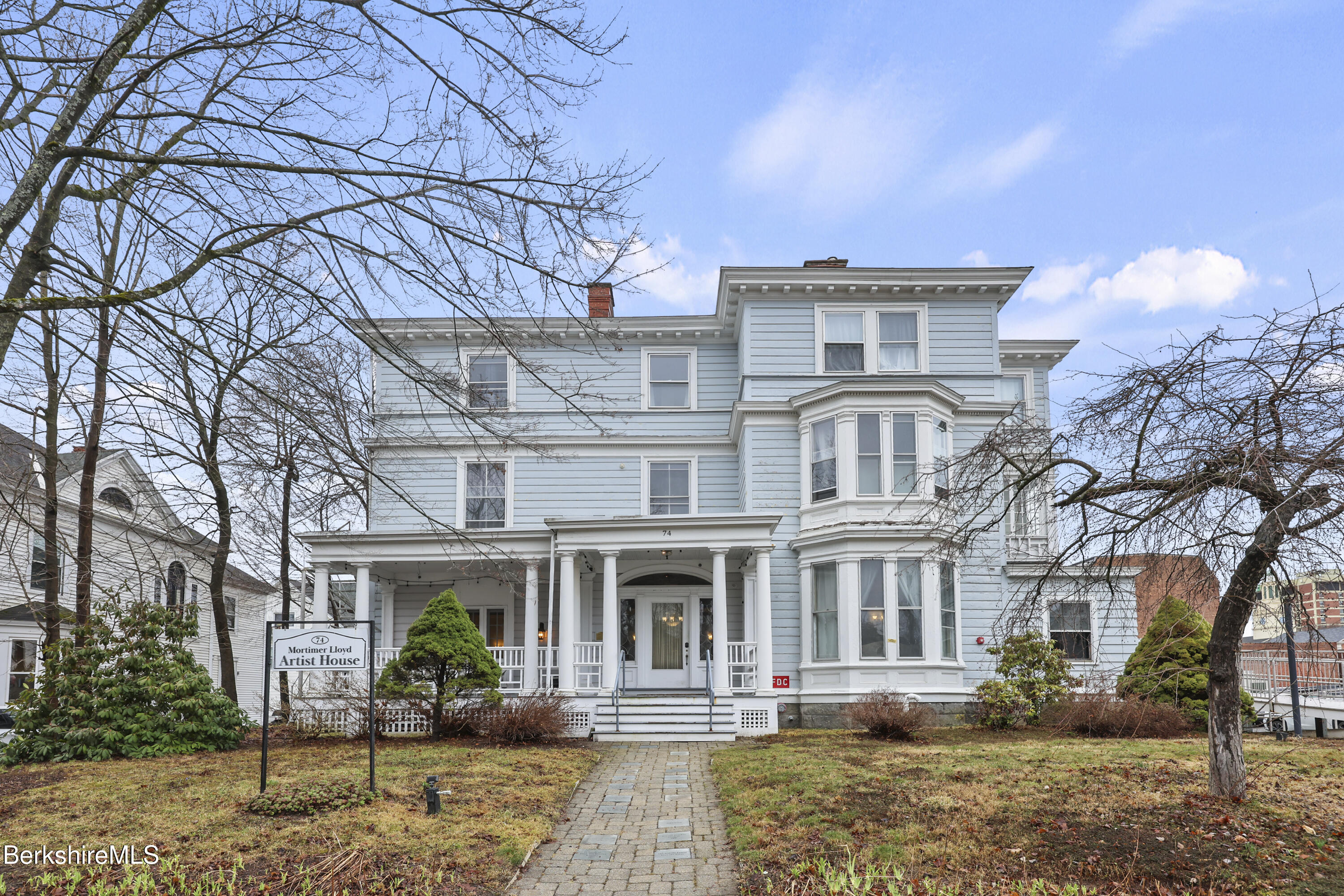 Light blue Mortimer Lloyd Artist House with a columned porch and projecting bay windows.