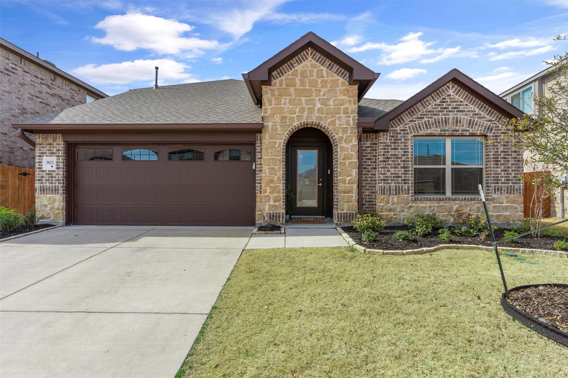 Brick and stone house with an arched entry, dark double garage door, and broad driveway.