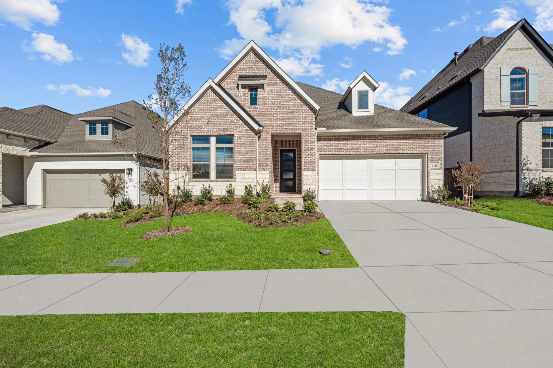 Brick house with a gabled facade, attached garage, landscaped lawn, and broad driveway.