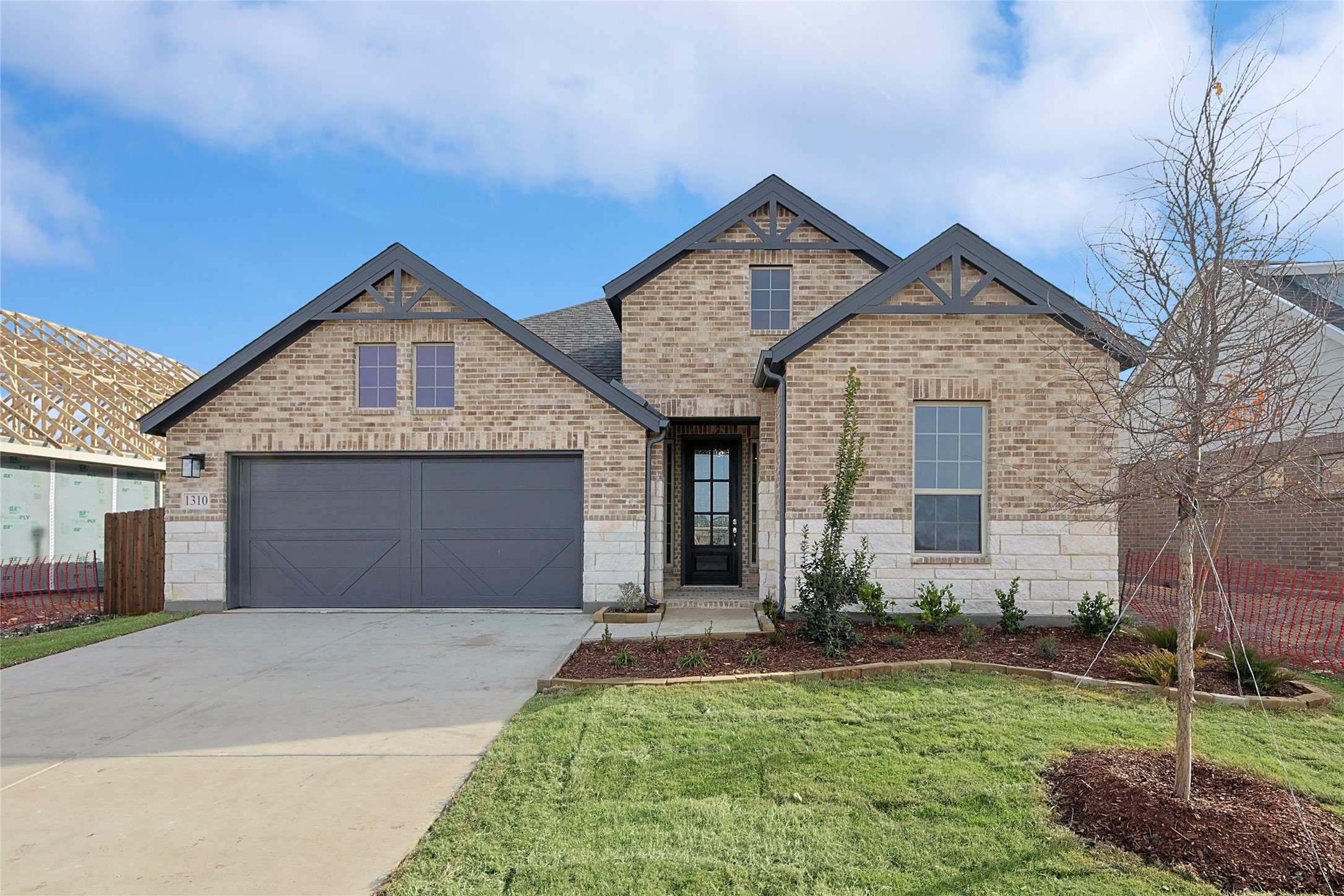 Two-story brick house with dark gabled roofs, a two-car garage, and a landscaped front yard.