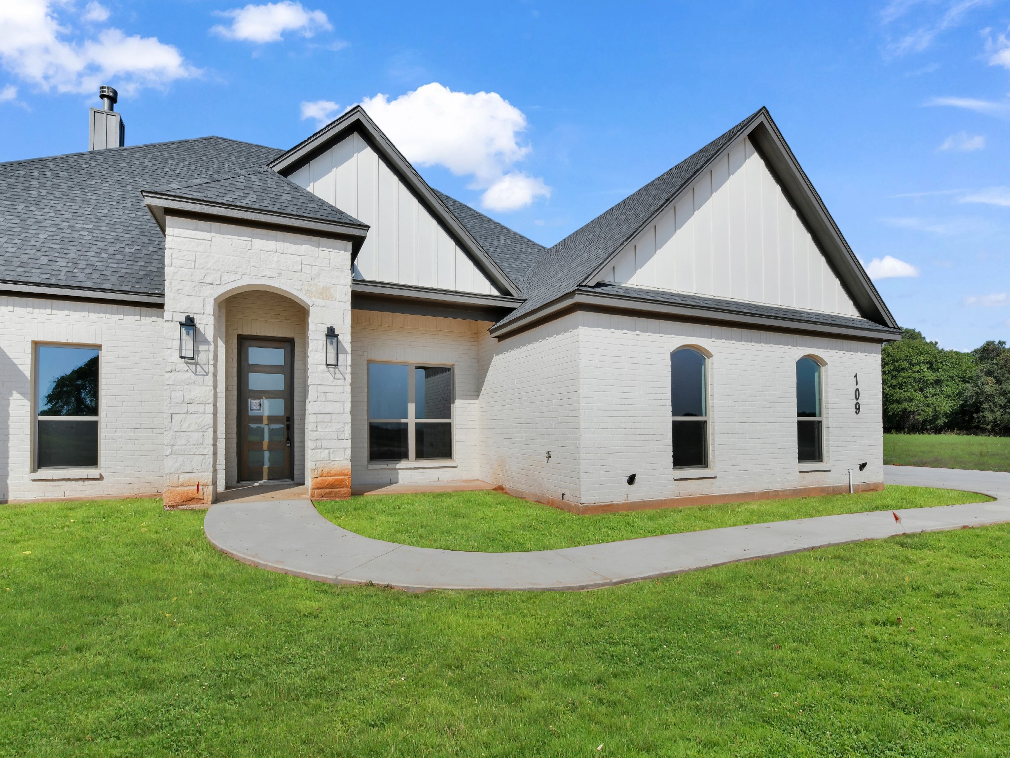 White brick house with steep gabled roofs, an arched entryway, and a curved walkway across the lawn.