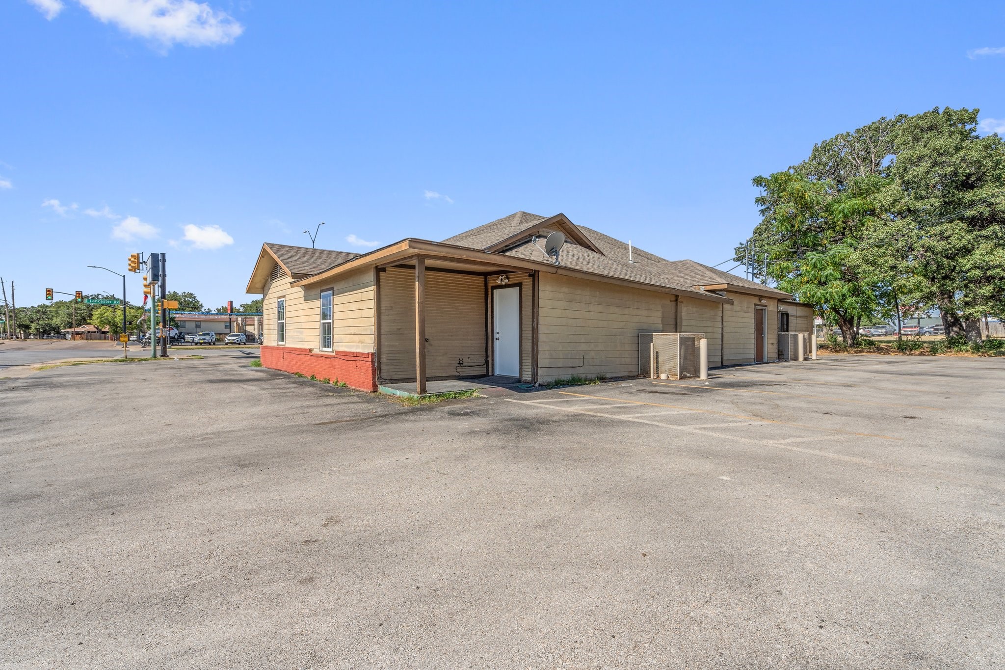 Tan single-story building with a red lower facade beside a large paved parking lot.