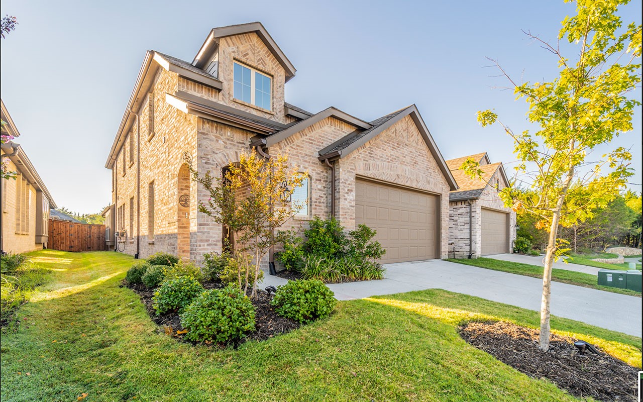 Two-story brick house with an upper dormer, two-car garage, and landscaped front yard.