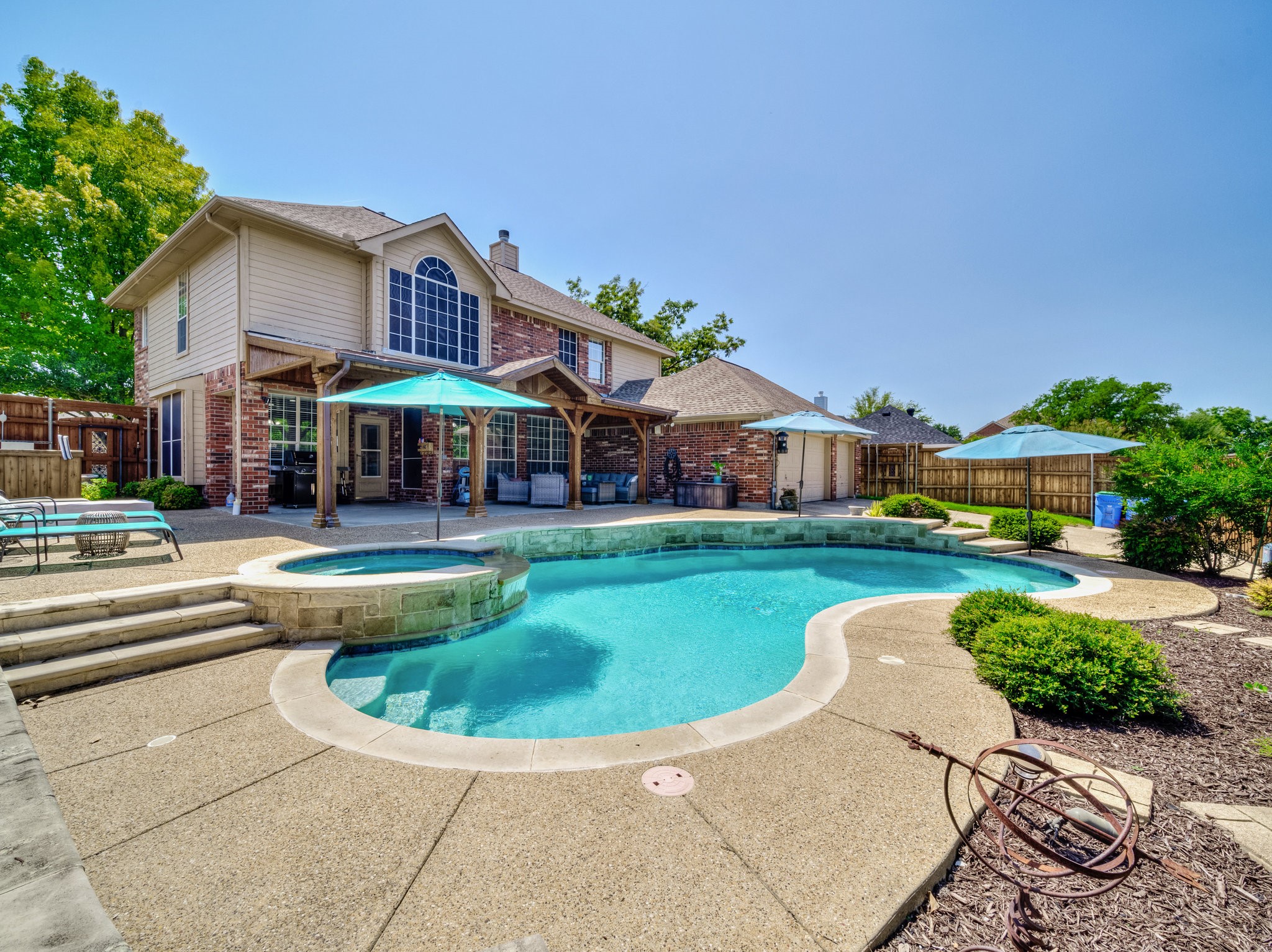 Backyard pool and raised spa beside a two-story brick house with a covered patio.