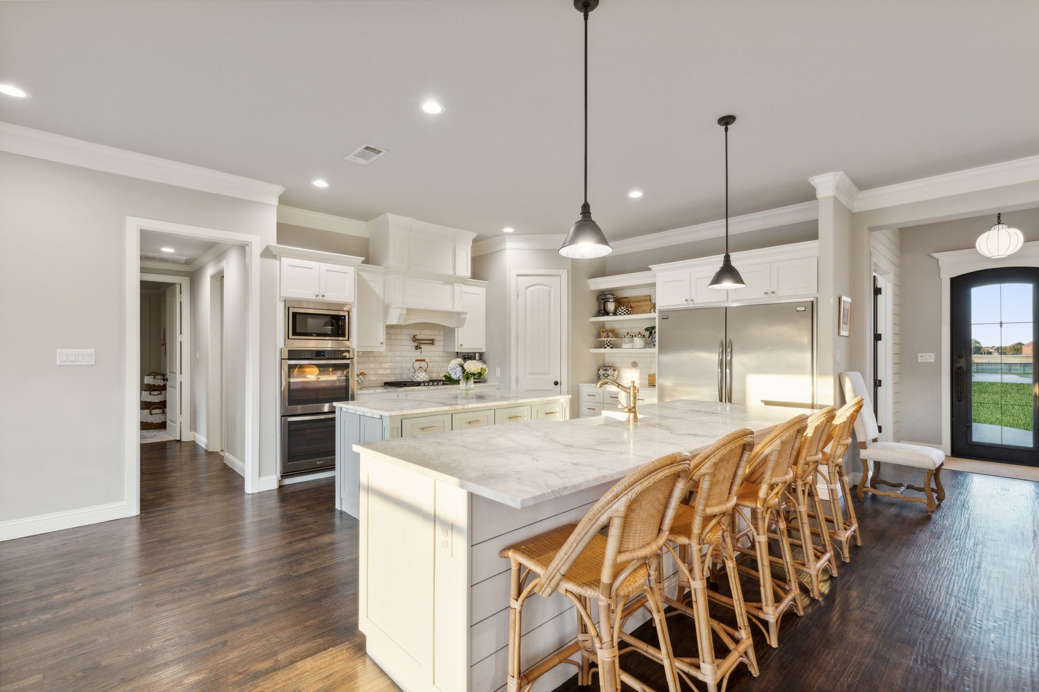 Bright kitchen with white cabinetry, marble island, stainless appliances, and woven stools.