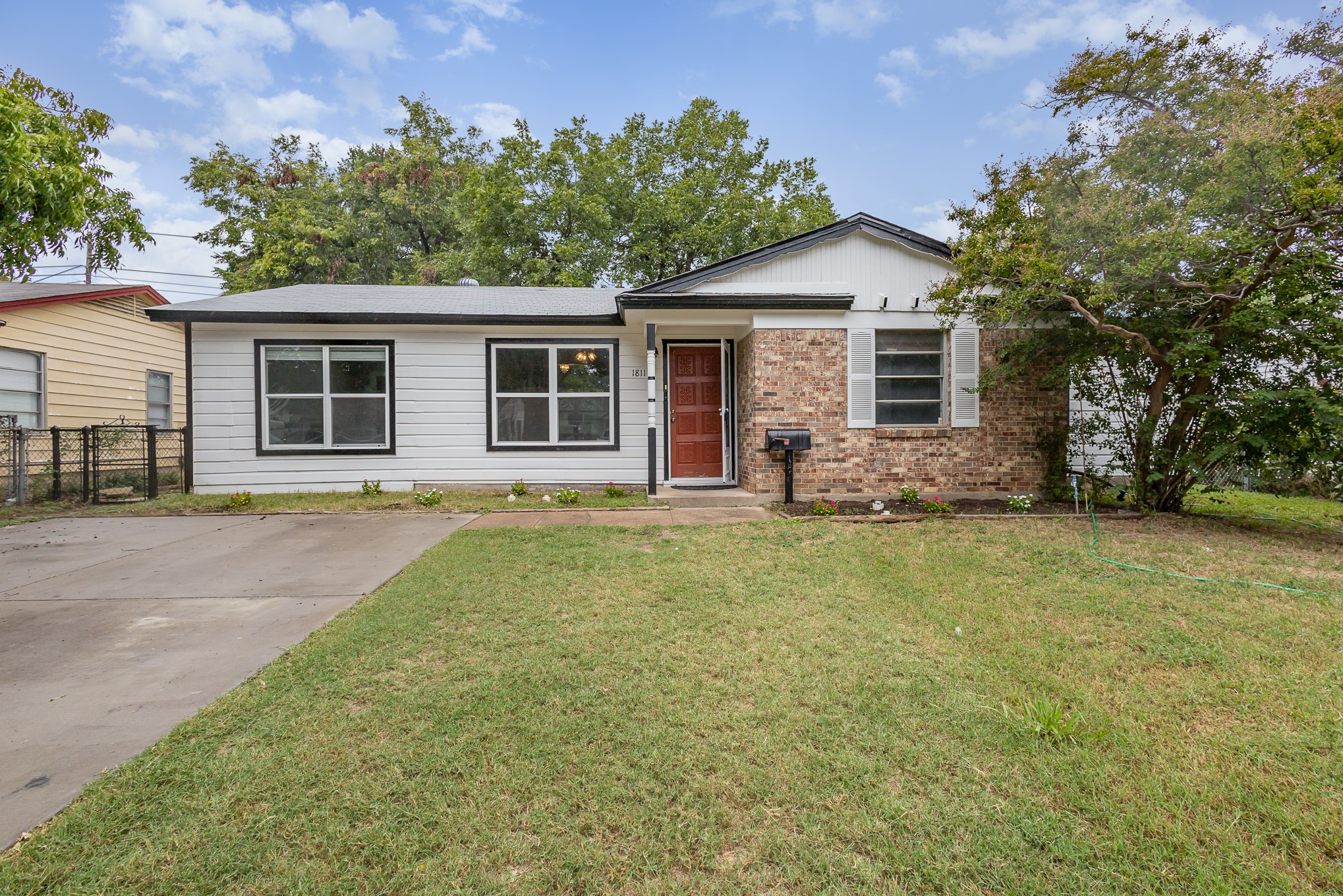 Single-story house with white siding, brick facade, red front door, and a wide front lawn.