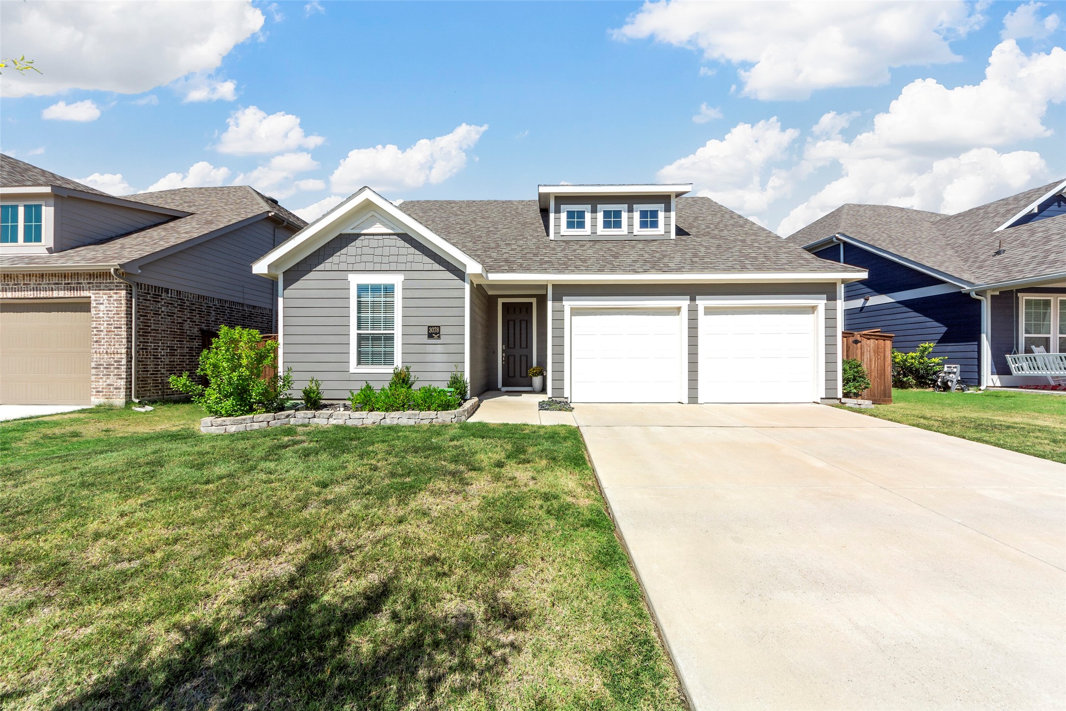 Gray single-story home with two white garage doors, a broad driveway, and landscaped front lawn.