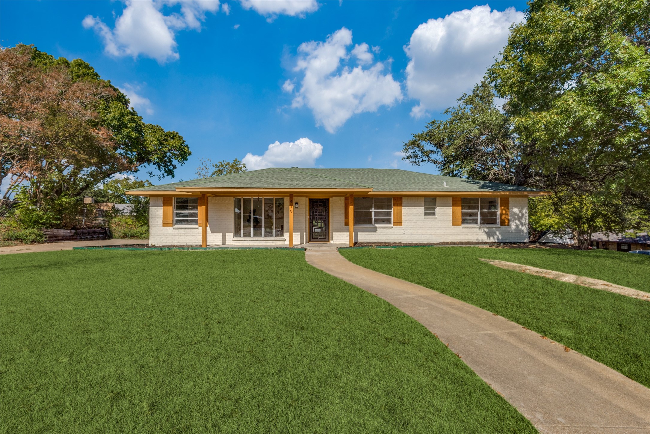 Single-story white brick home with wooden shutters, a broad lawn and a curved walkway to the front door.