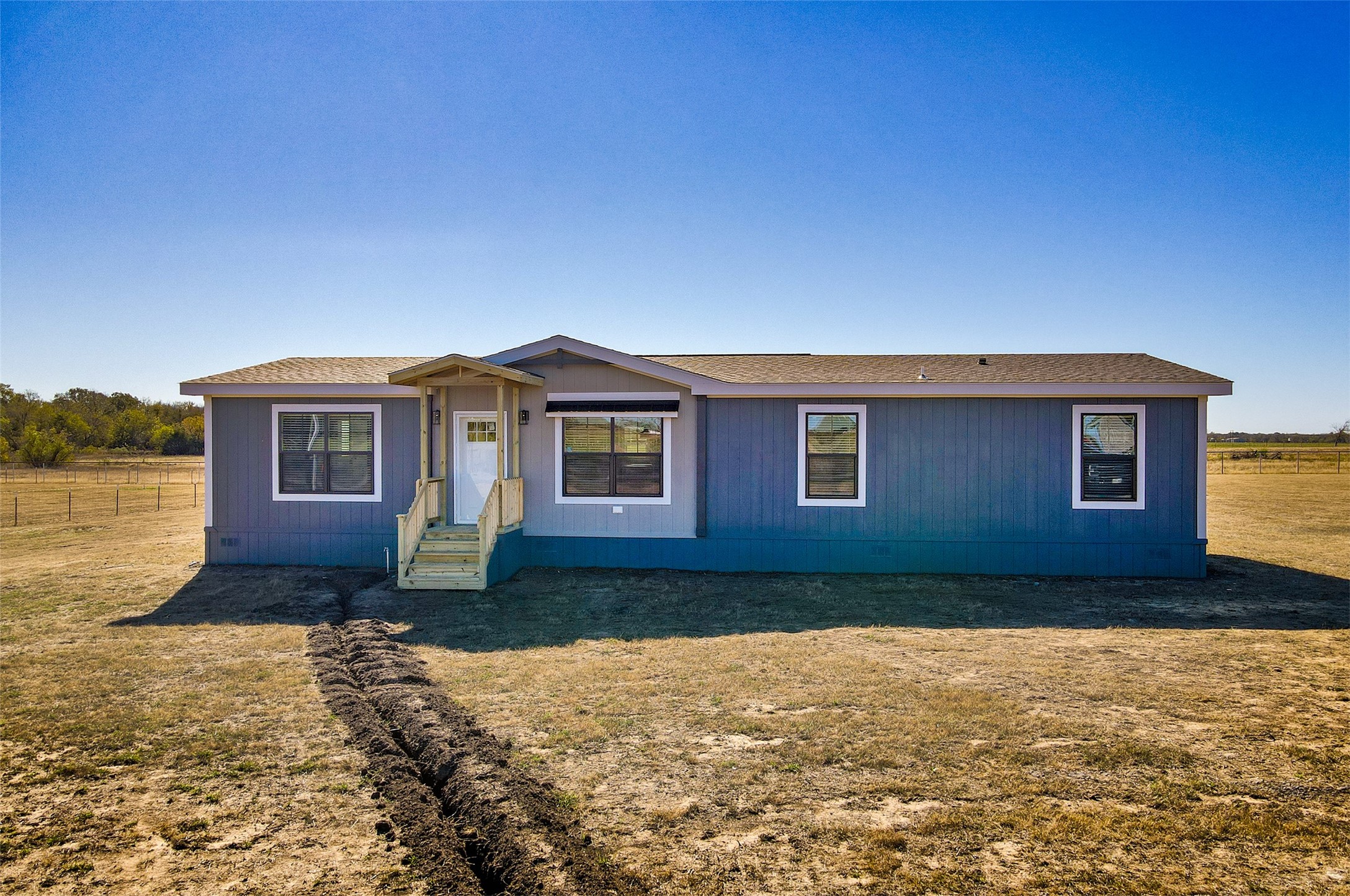 Blue single-story home with a covered porch on an open, fenced rural lot.