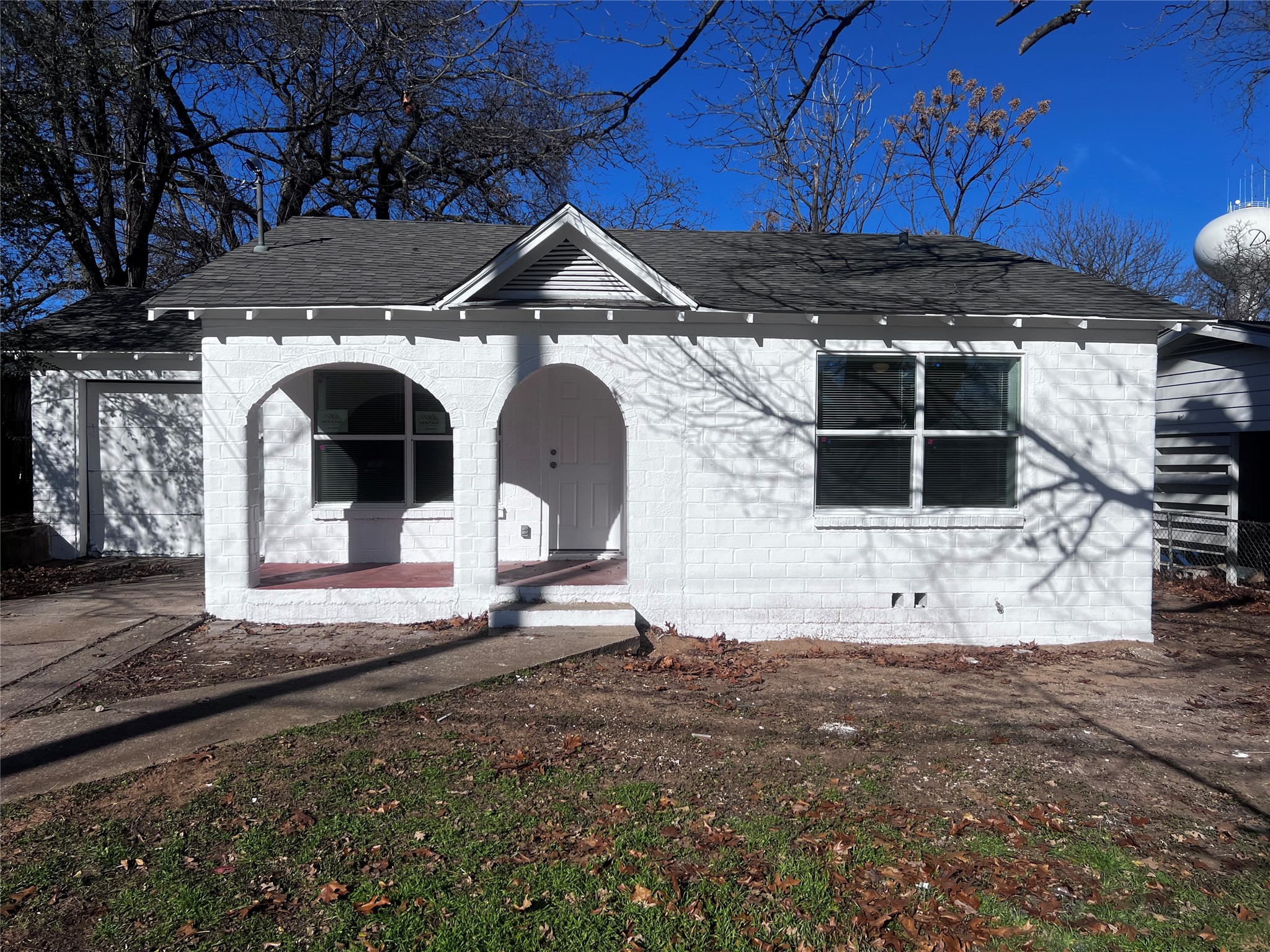 White brick house with arched porch openings and a dark shingle roof.