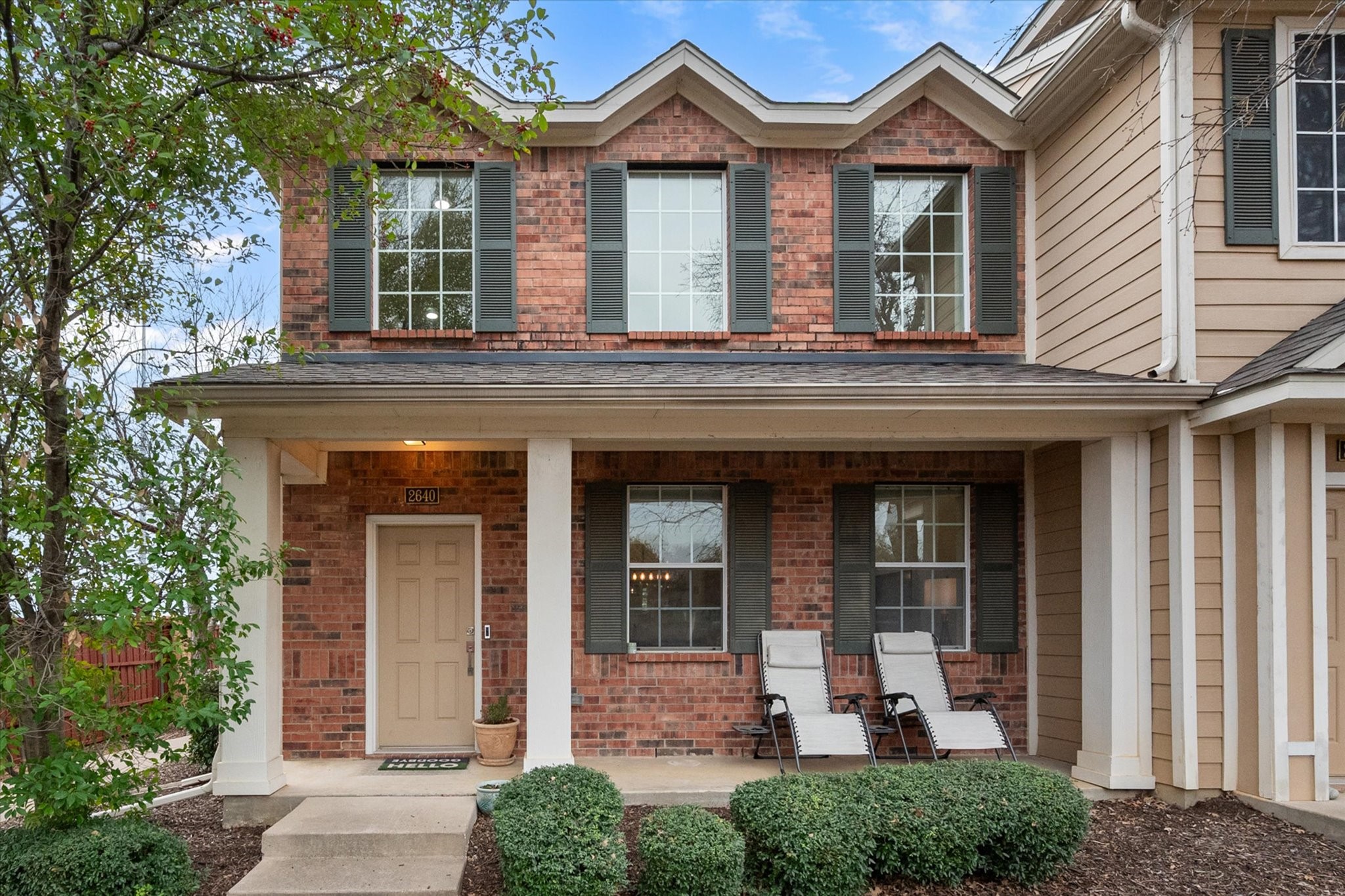 Two-story brick house with a covered porch, dark shutters, and two lounge chairs.