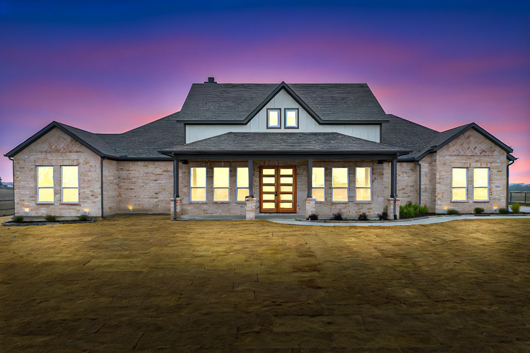 Stone-faced house with a central gable and glowing windows beneath a colorful dusk sky.