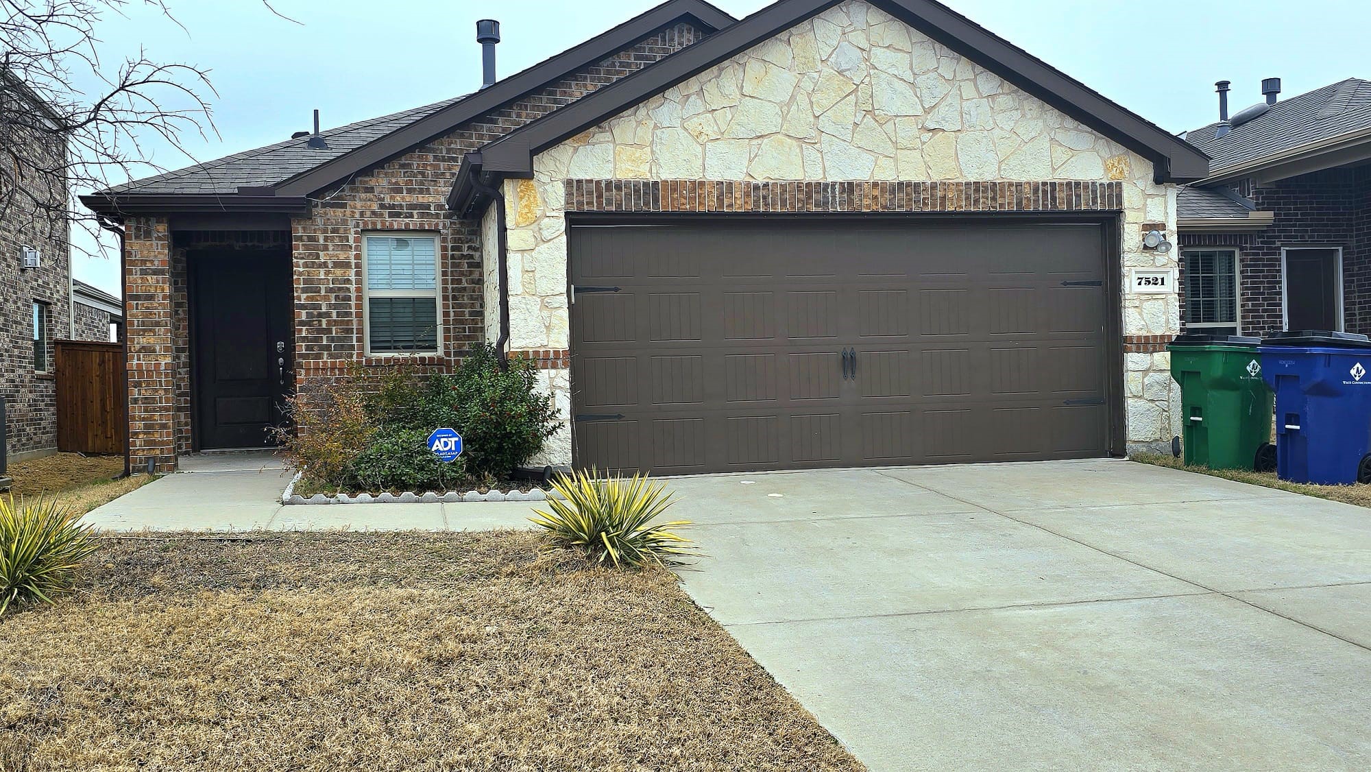 Single-story stone-and-brick house with a dark double garage door and wide concrete driveway.
