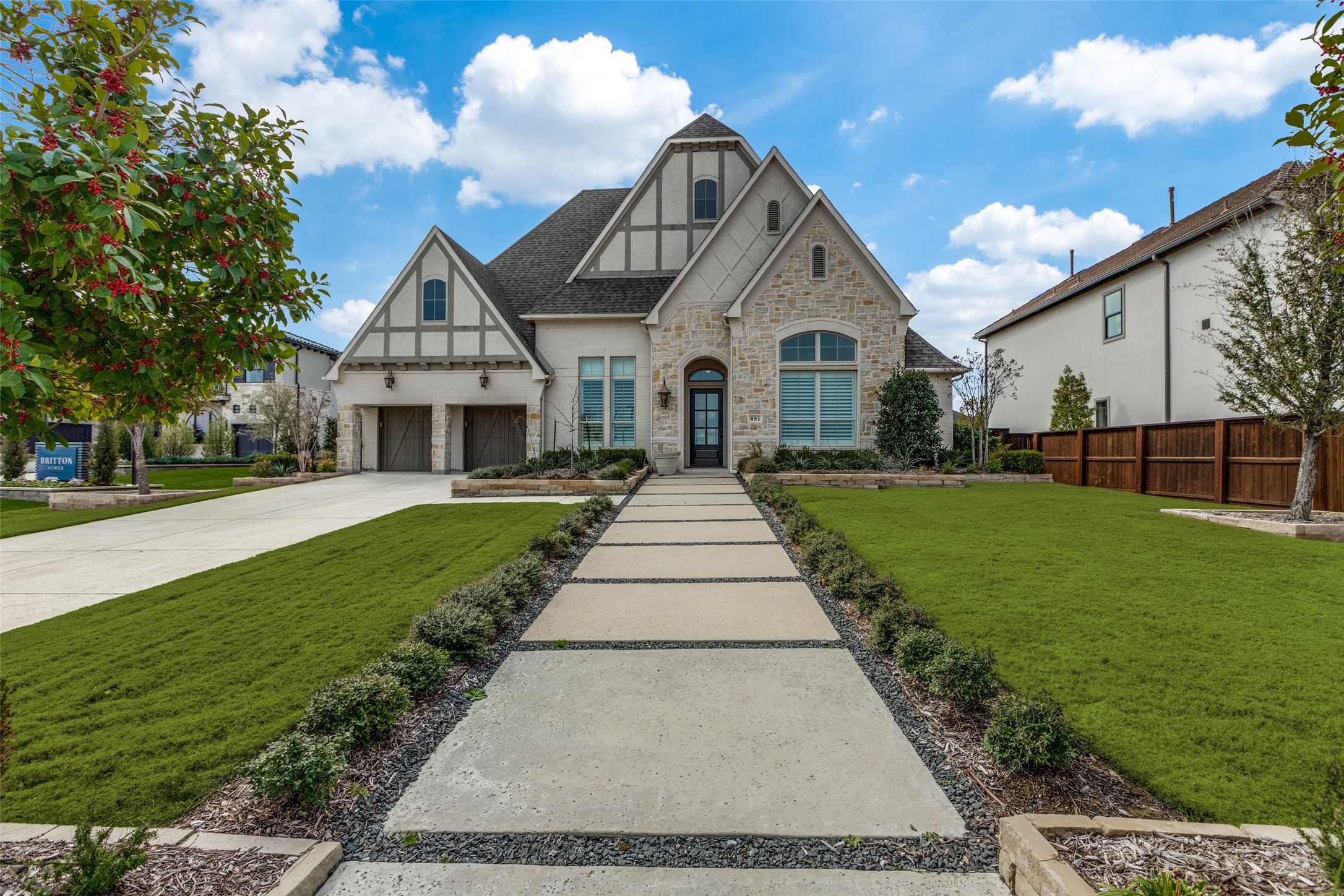 Two-story stone-and-timber home with a double garage, landscaped lawn, and wide walkway to the entrance.