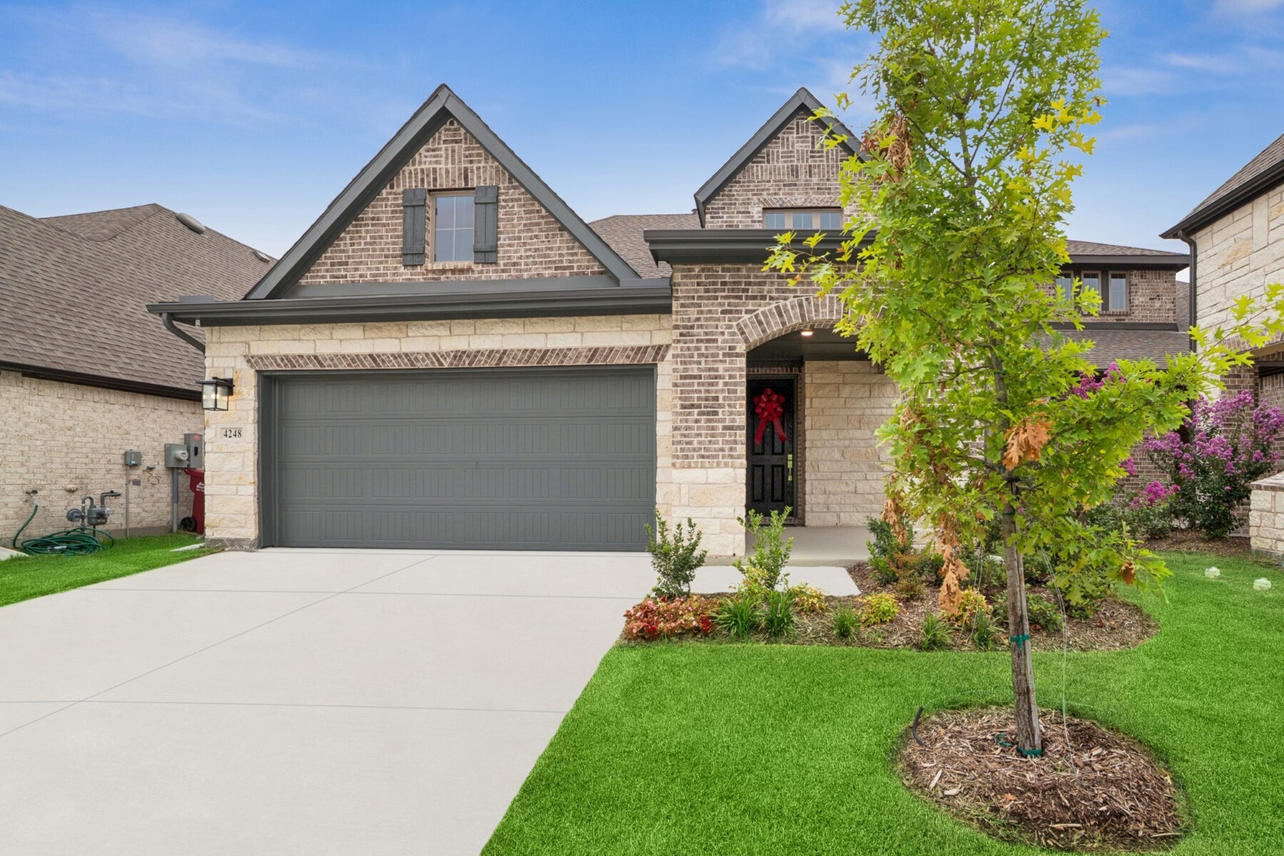 Two-story brick-and-stone home with a wide garage, landscaped lawn, and tree partly screening the entrance.