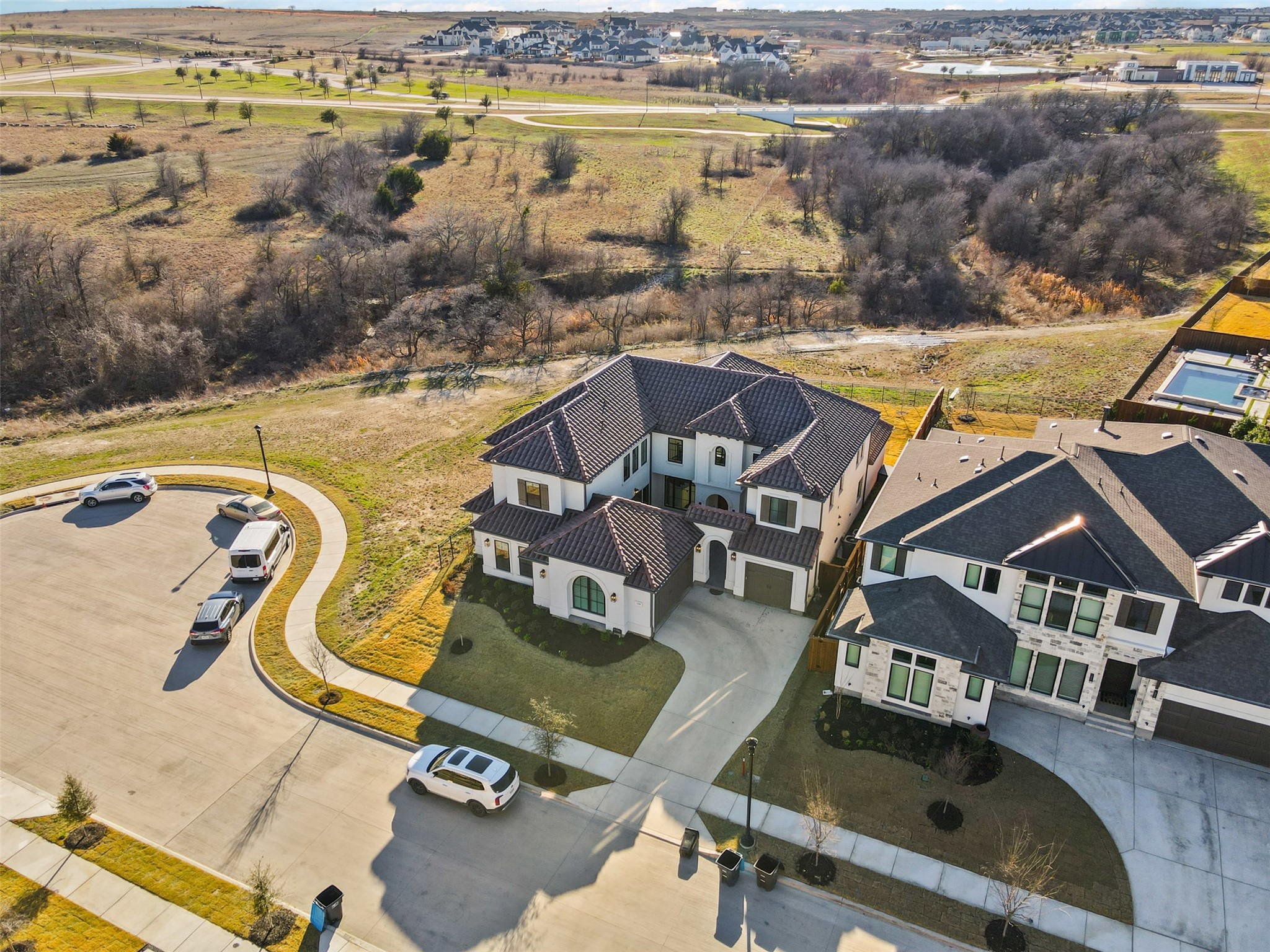 Aerial view of a large white home on a cul-de-sac beside a wooded greenbelt.