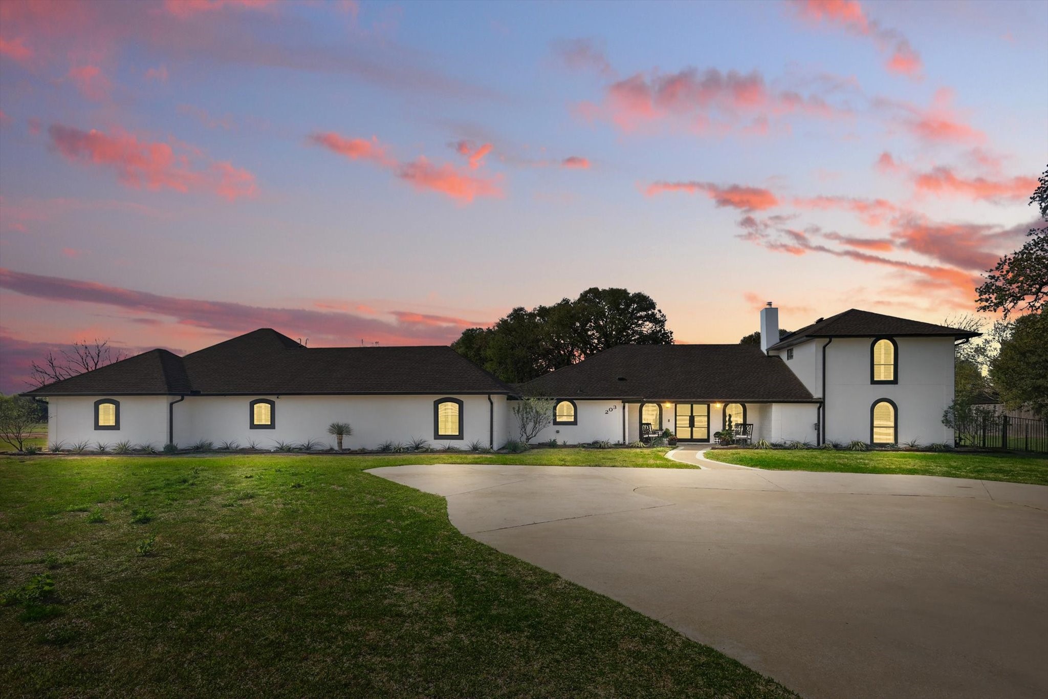 White two-story home with arched windows and a curved driveway beneath a pink sunset sky.