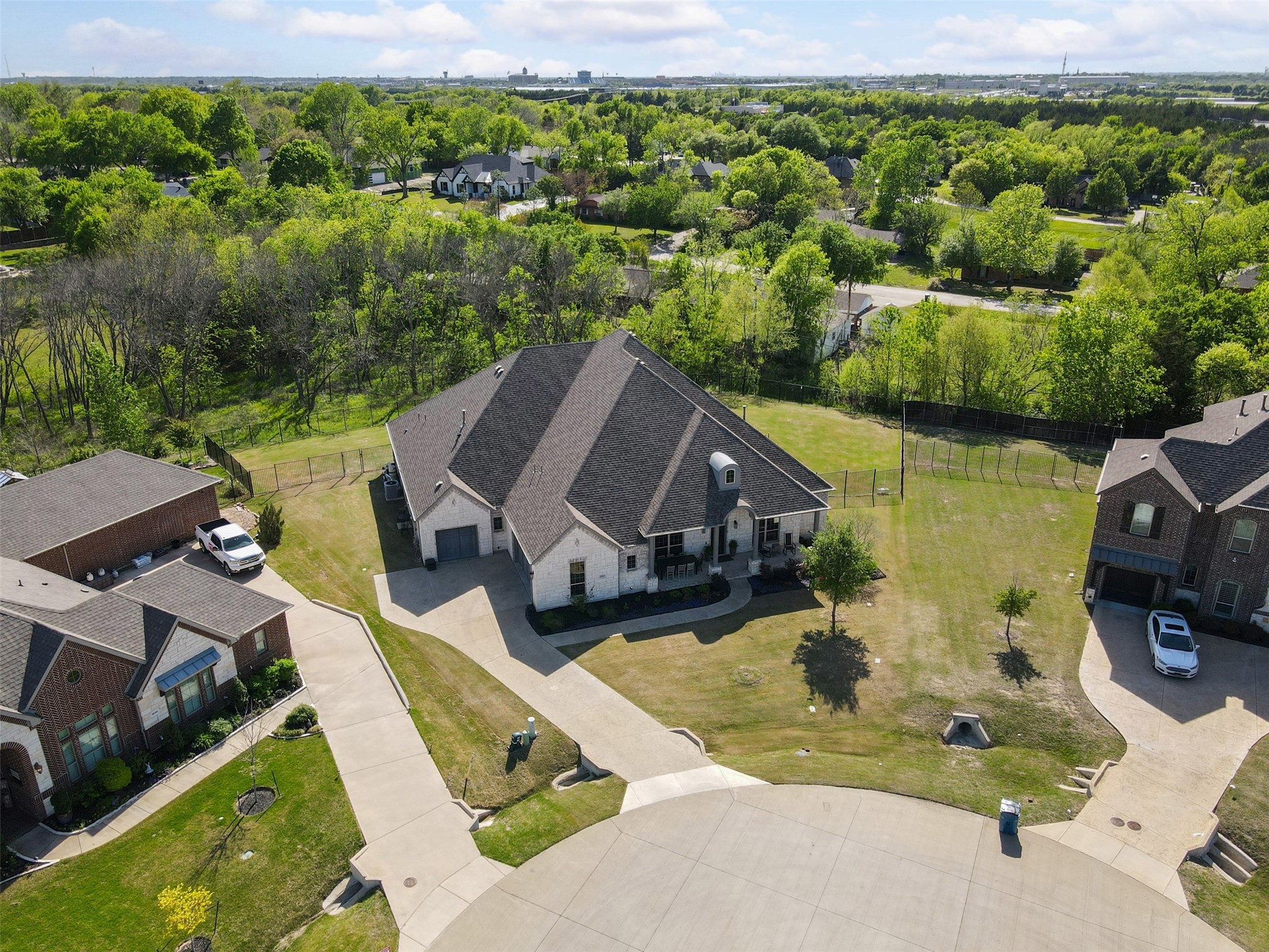 Aerial view of a light stone house with a dark multi-gabled roof and fenced lawn on a cul-de-sac.