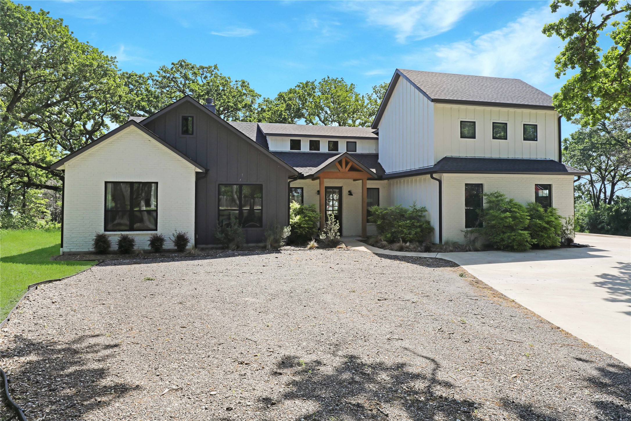 Modern two-story home with white and charcoal exterior, timber entry, and broad gravel forecourt.