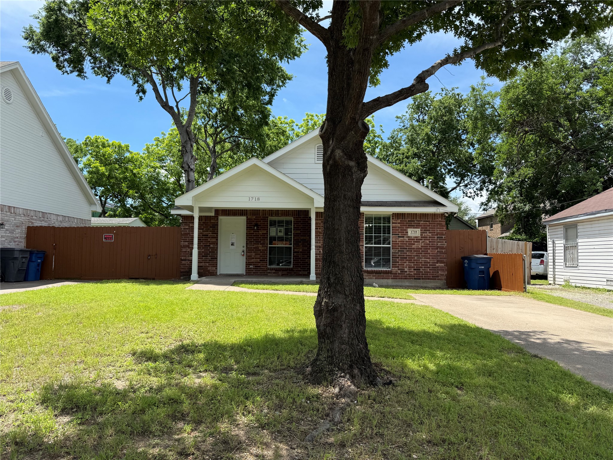 Brick house with white gabled entry, partly obscured by a large tree in the grassy front yard.