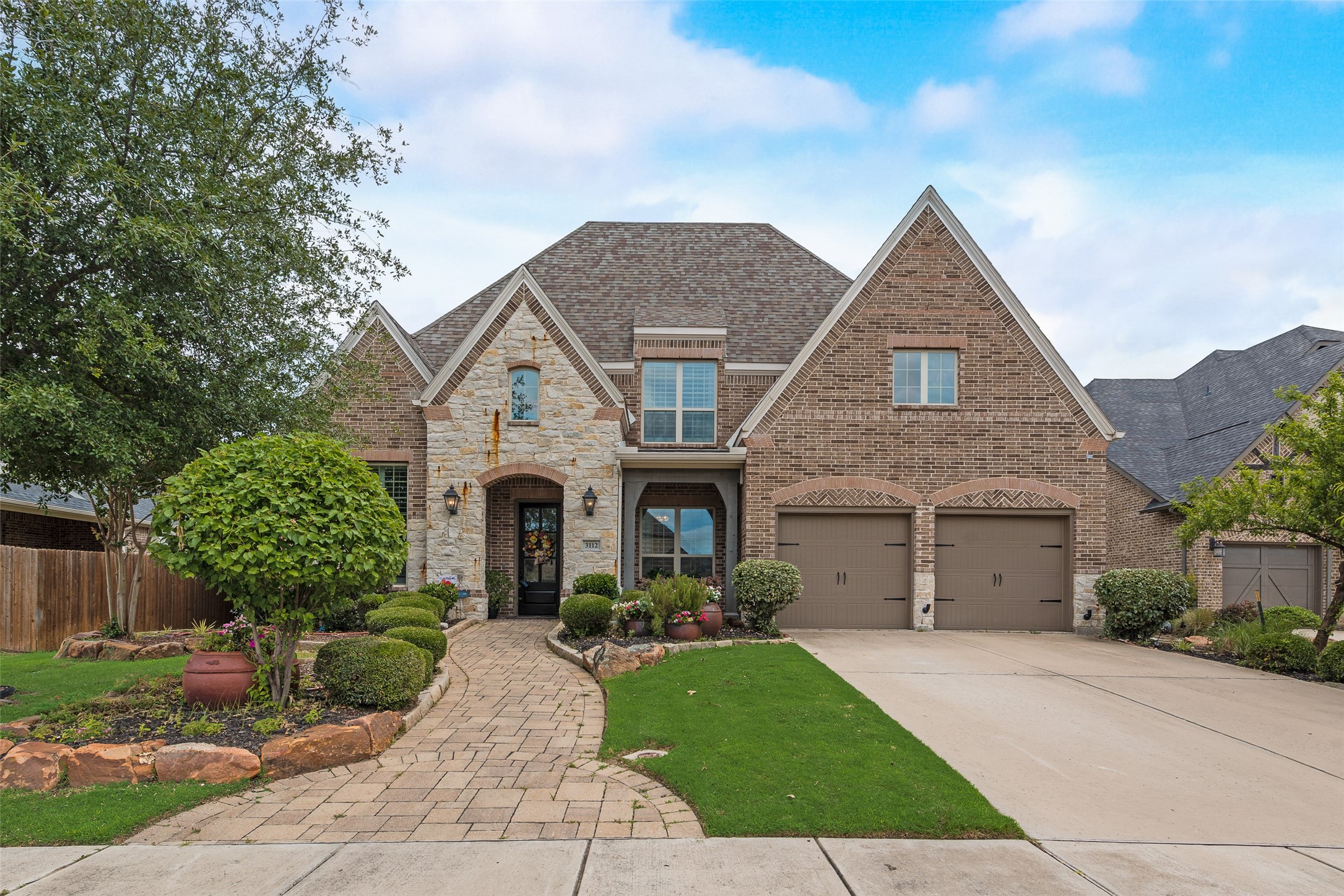 Two-story brick and stone home with twin garages and a curved landscaped walkway.