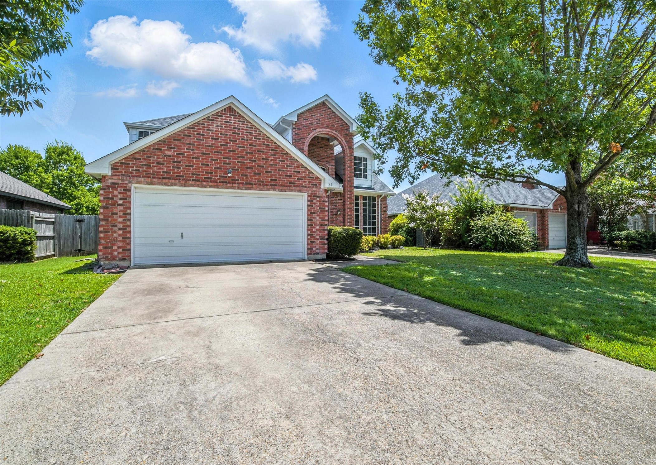 Two-story brick house with an attached garage, wide driveway, and mature trees.