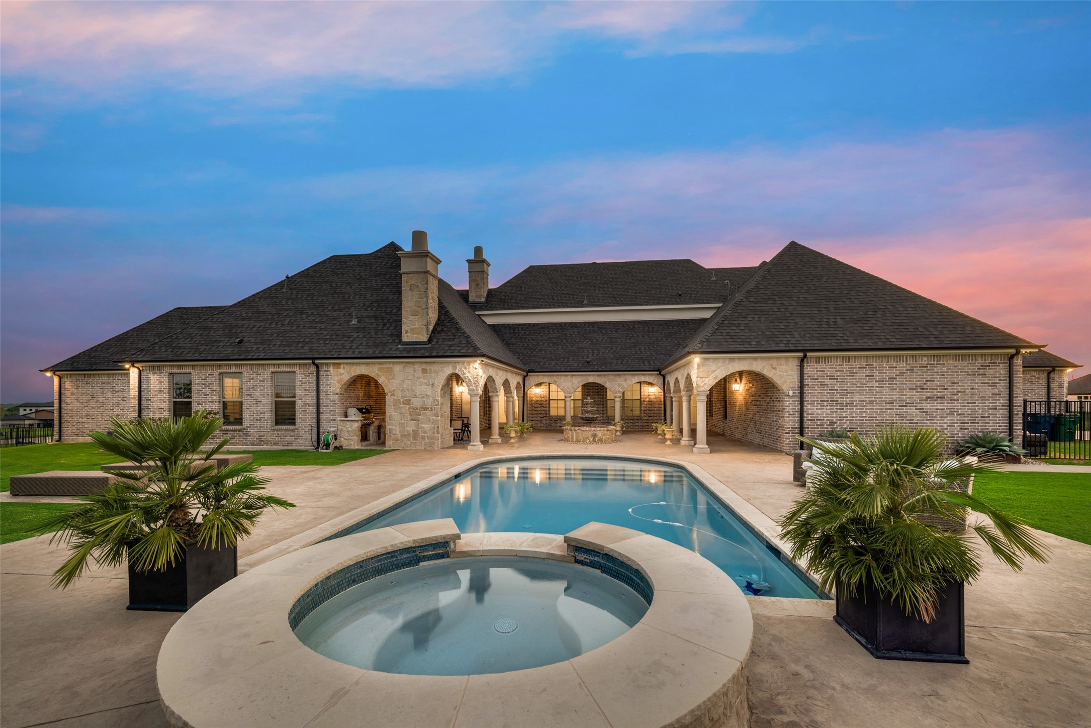Backyard pool and raised circular spa in front of a brick-and-stone home at dusk.