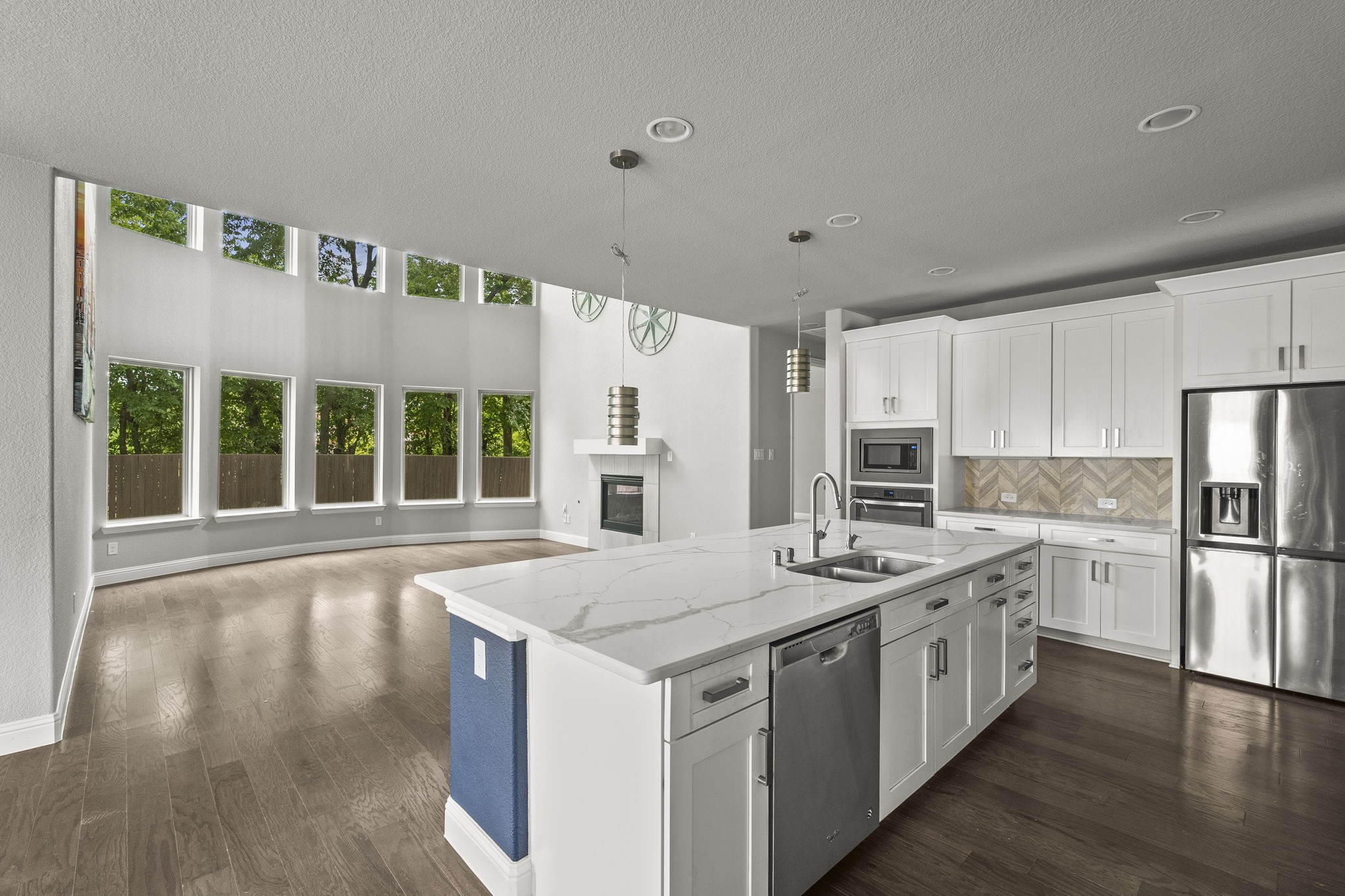 Open kitchen with a large white island, stainless steel appliances, and tall windows overlooking trees.