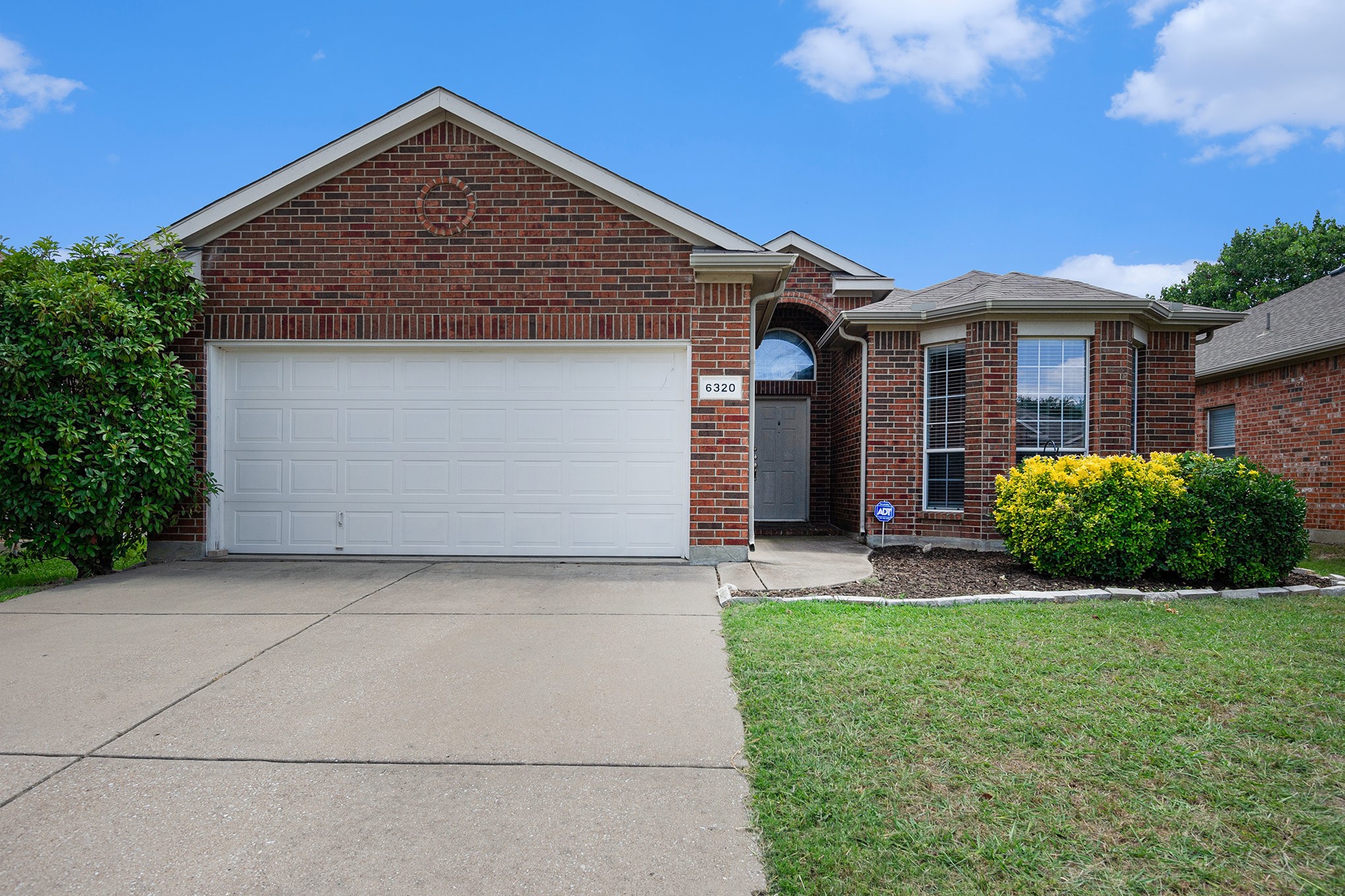 Red-brick house with a white double garage door, arched entry, and landscaped front lawn.