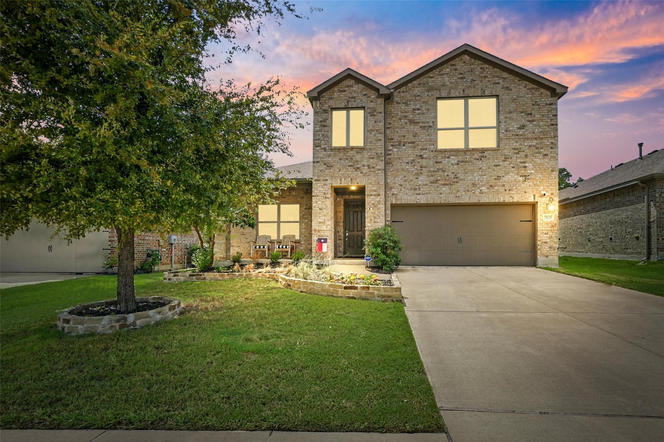 Two-story brick house with a two-car garage and landscaped lawn at dusk.