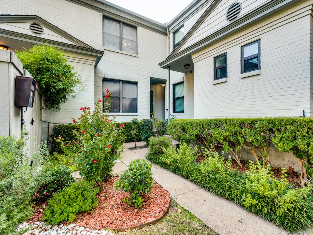 White brick residence with a landscaped courtyard, walkway, and flowering roses.