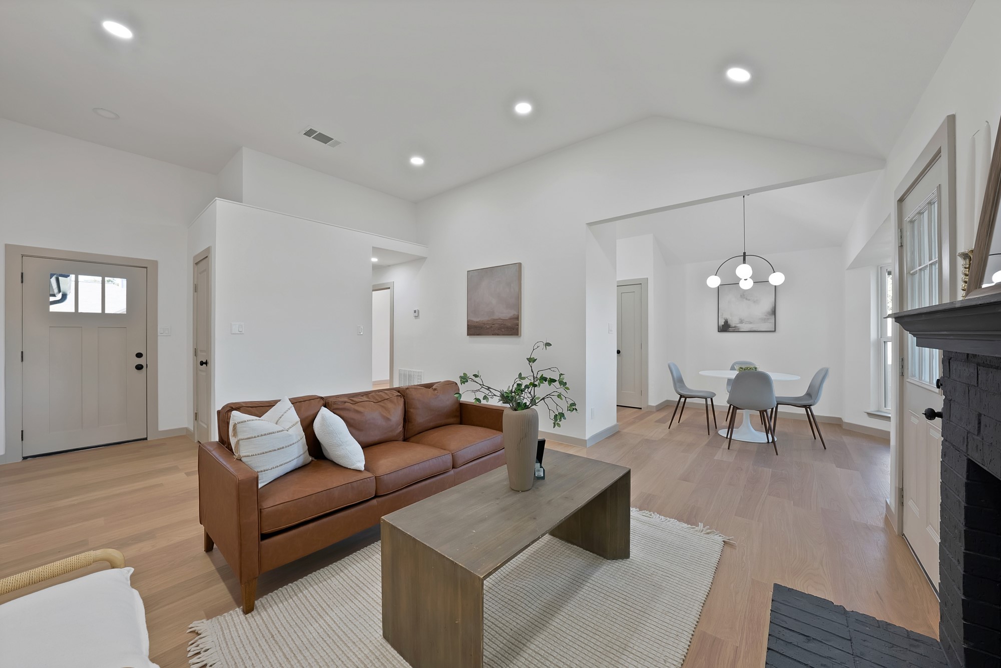 Open-plan living and dining room with a brown leather sofa and black fireplace.