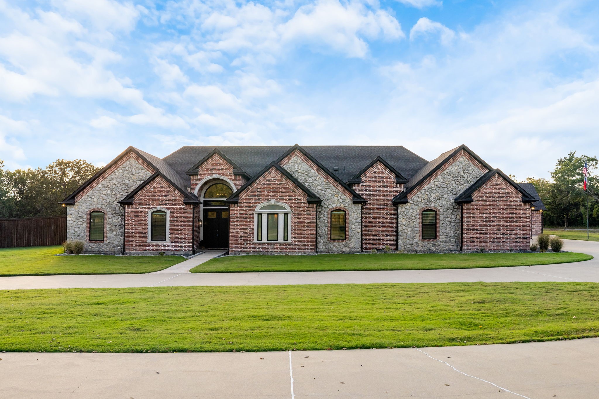 Brick-and-stone house with multiple gables, a central arched entry, and a broad front lawn.