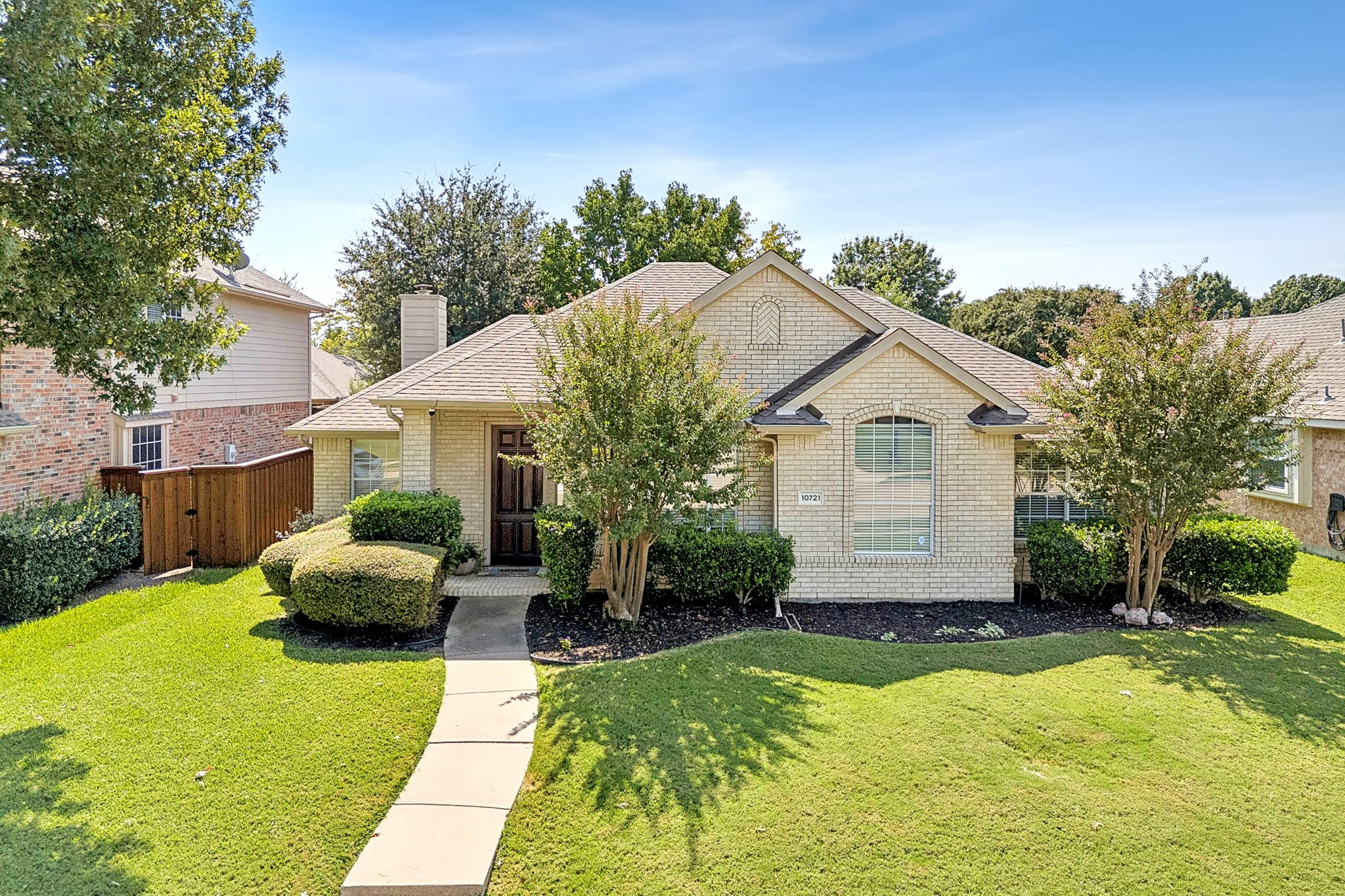 Light brick house with a gabled roof, trimmed landscaping, and a curved walkway across the lawn.