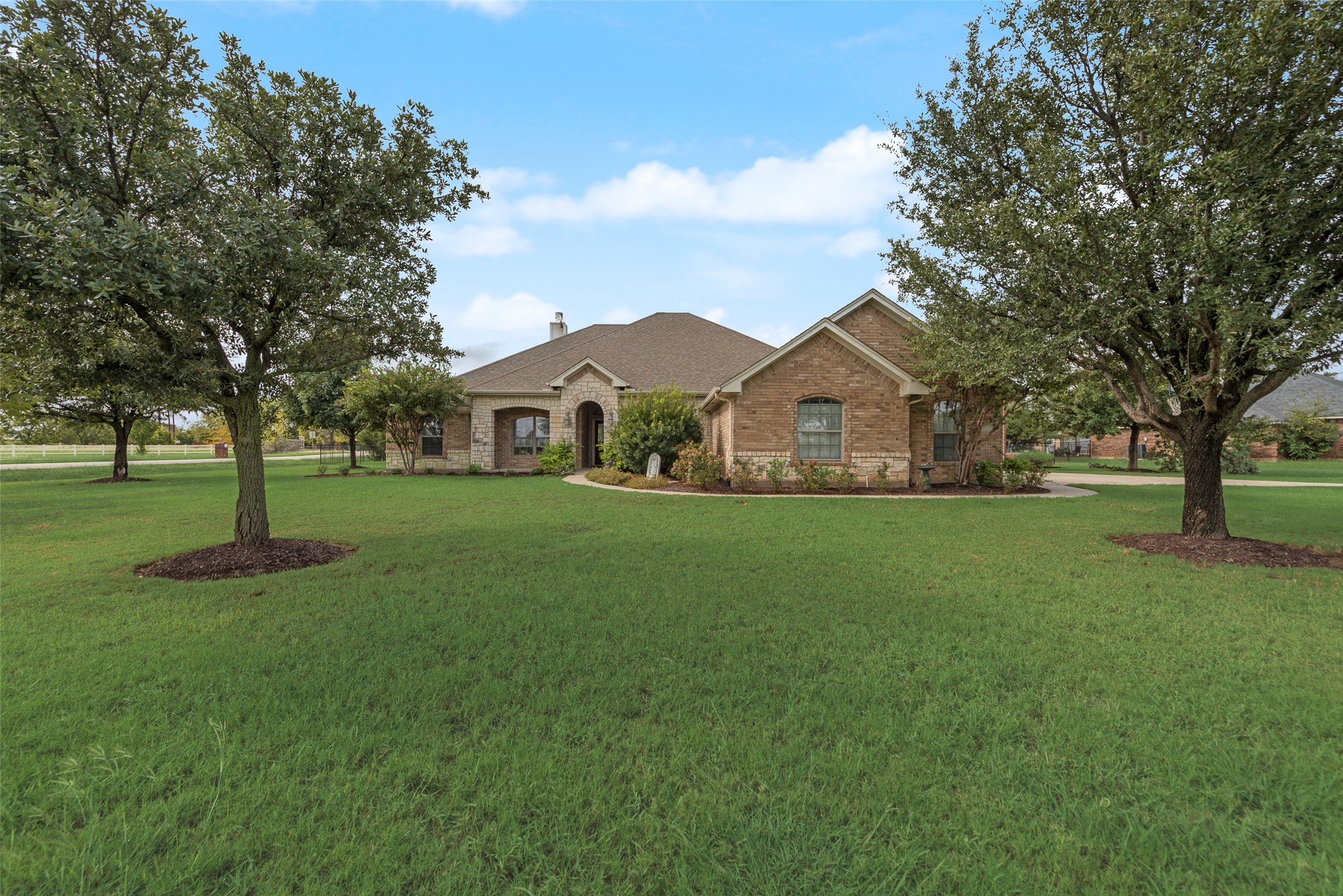 Brick-and-stone home set behind a broad lawn, framed by mature trees.
