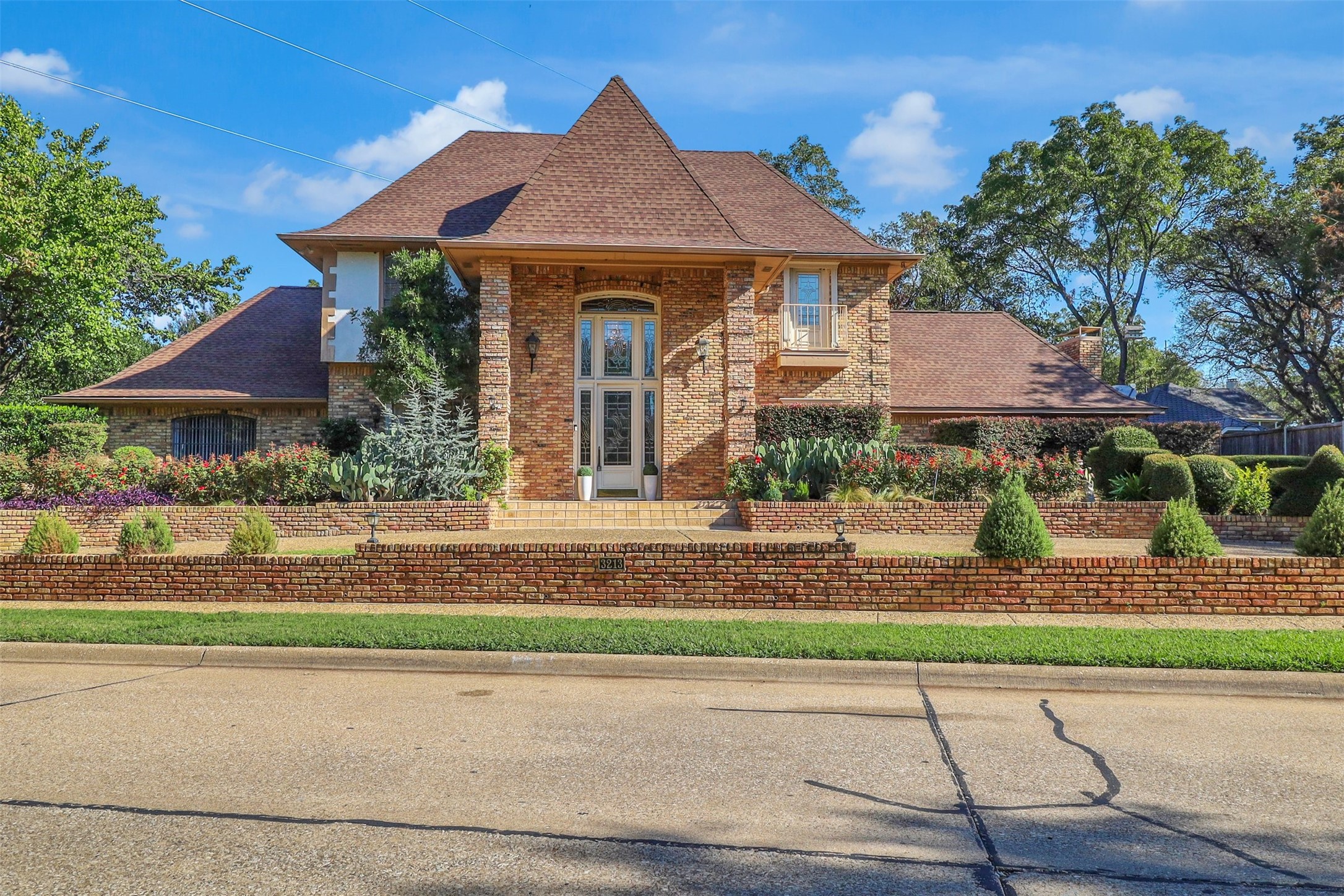 Two-story brick house with a steep roof, landscaped garden, and low brick front wall.