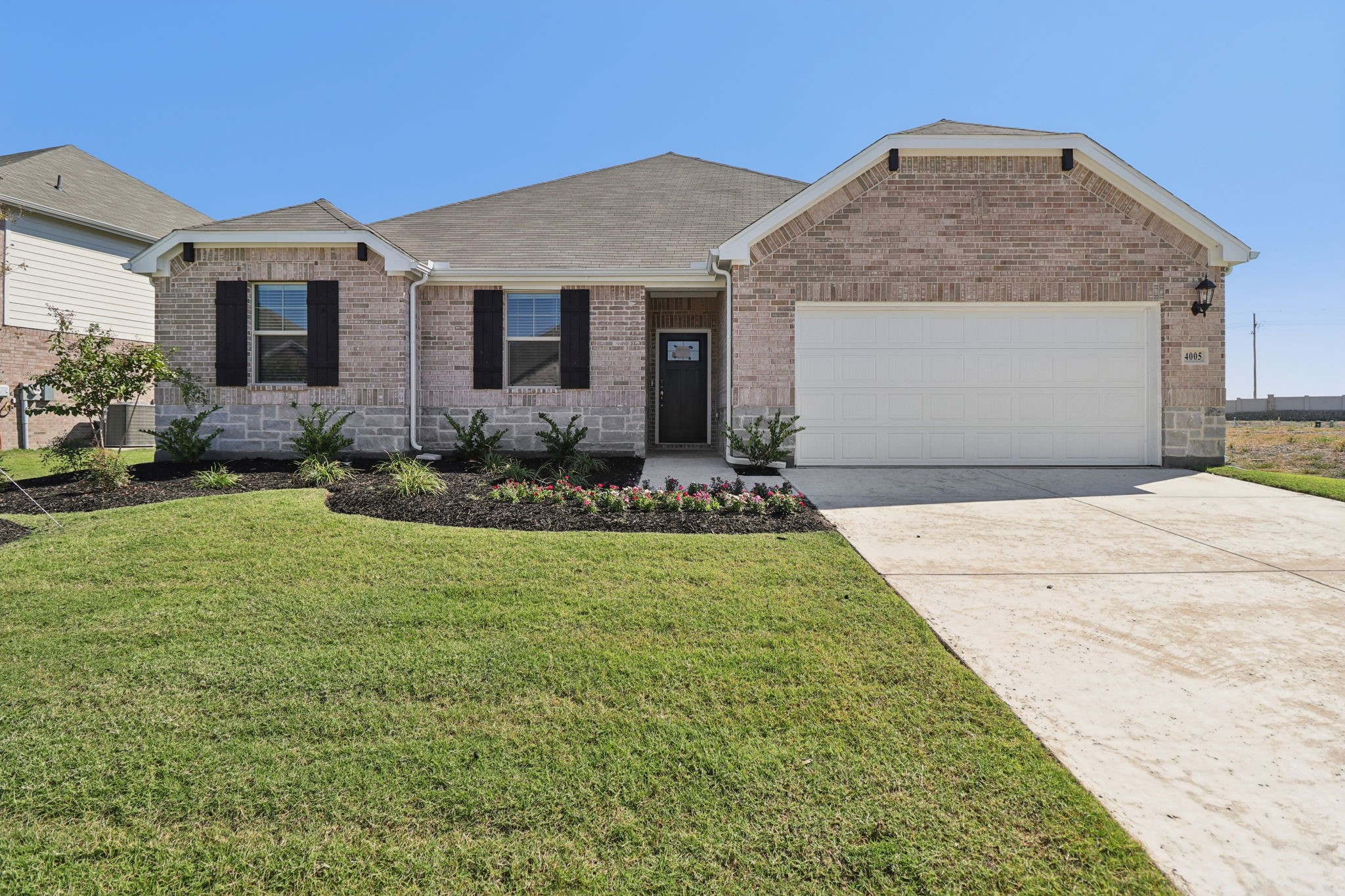 Brick house with a two-car garage, landscaped flower beds, and a broad front lawn.