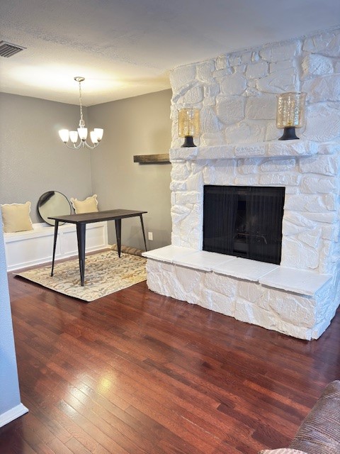 Living room with a white stone fireplace, hardwood floors, and a small table beneath a chandelier.