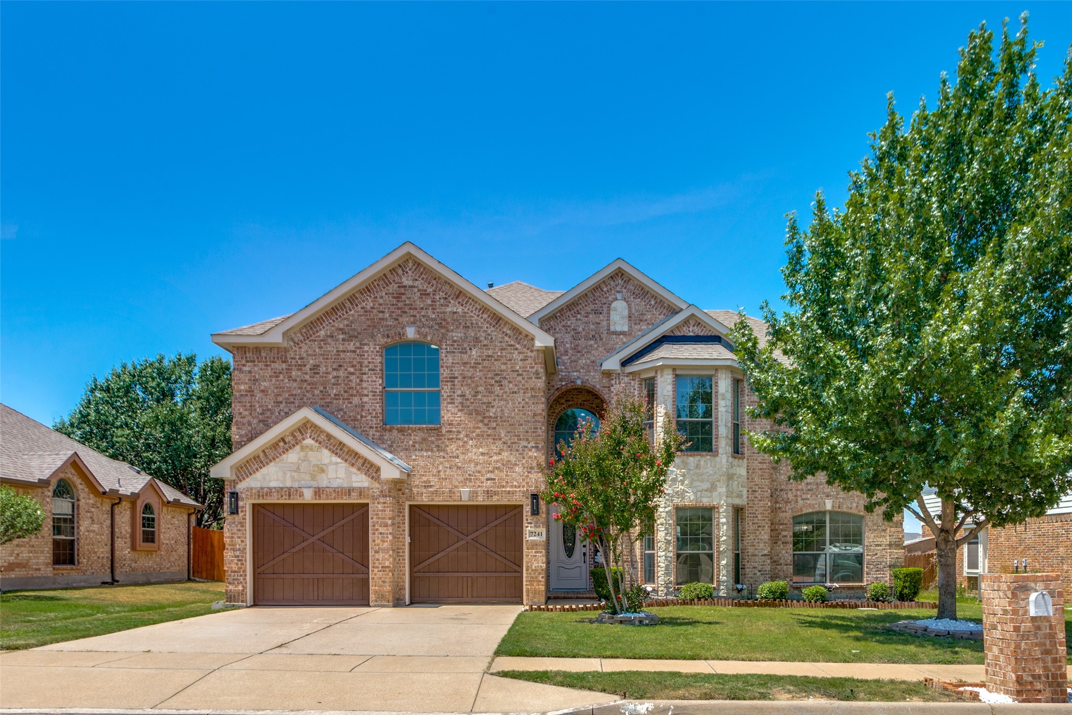 Two-story brick-and-stone house with twin garages, an arched entry, and mature trees.